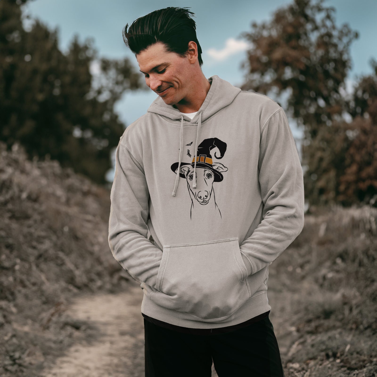 Hand-drawn sketch of Diva the Greyhound wearing a witch hat on a Cement Unisex pigment dyed hoodie, worn by a man