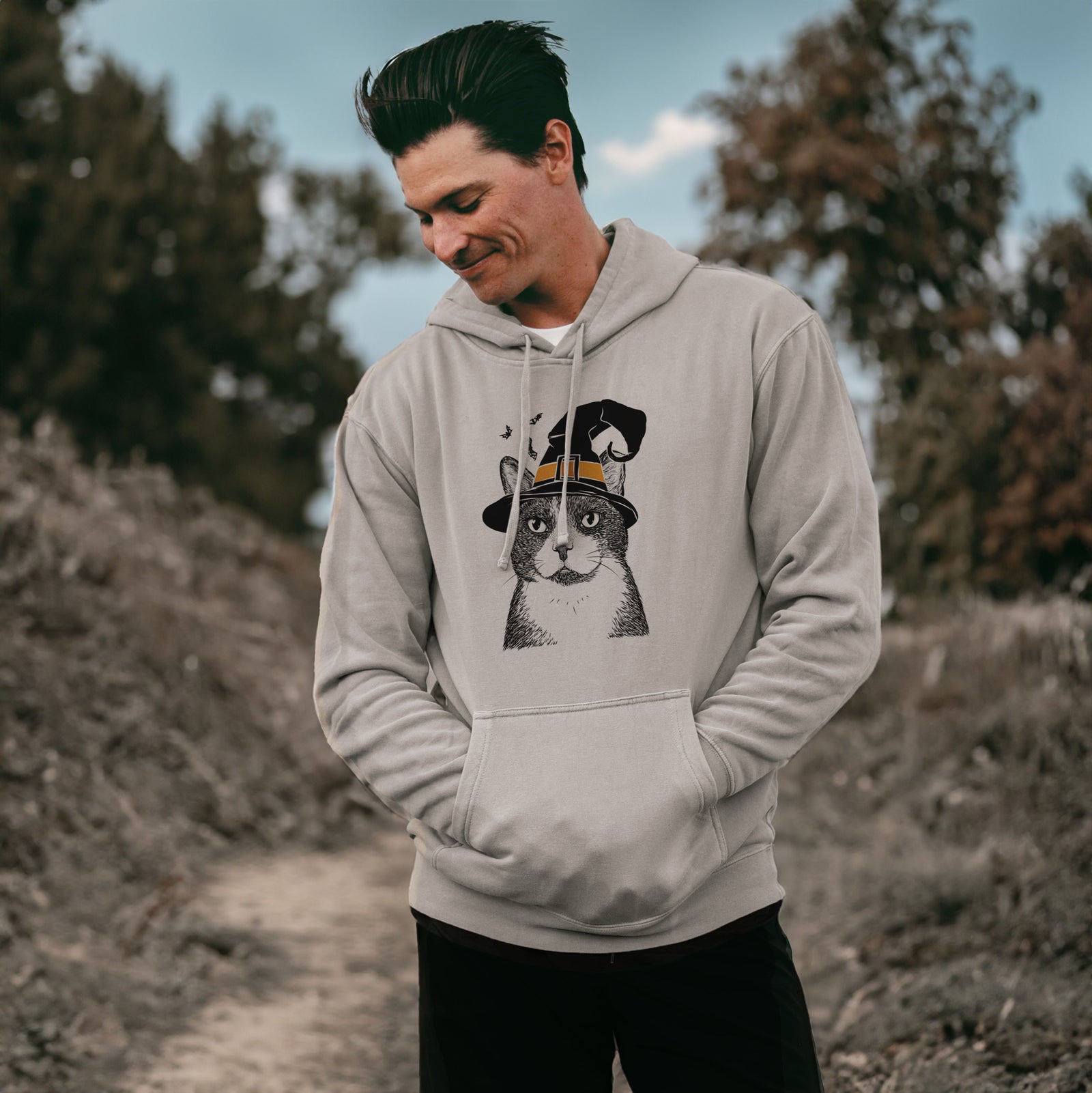 Hand-drawn sketch of Pinky the Tuxedo Cat wearing a witch hat on a Cement Unisex pigment dyed hoodie, worn by a man