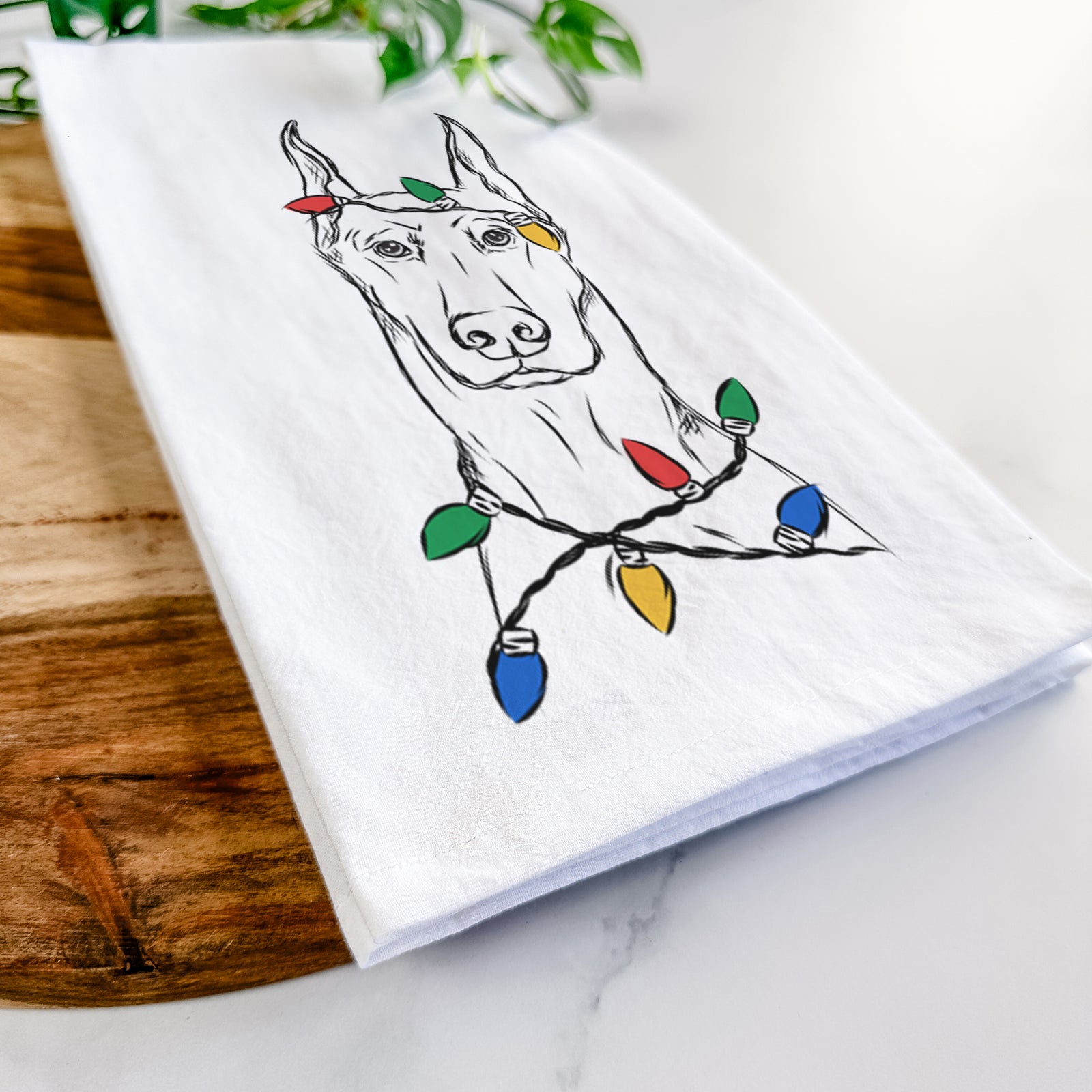 Hand-drawn sketch of Ace the Doberman Pinscher wrapped in Christmas lights on a tea towel