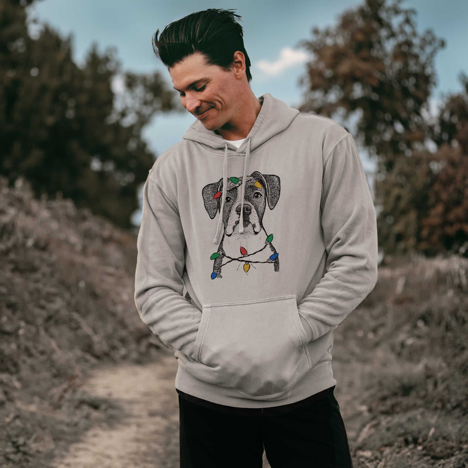Hand-drawn sketch of Annie the Boxer wrapped in Christmas lights on a Cement Unisex pigment dyed hoodie, worn by a man