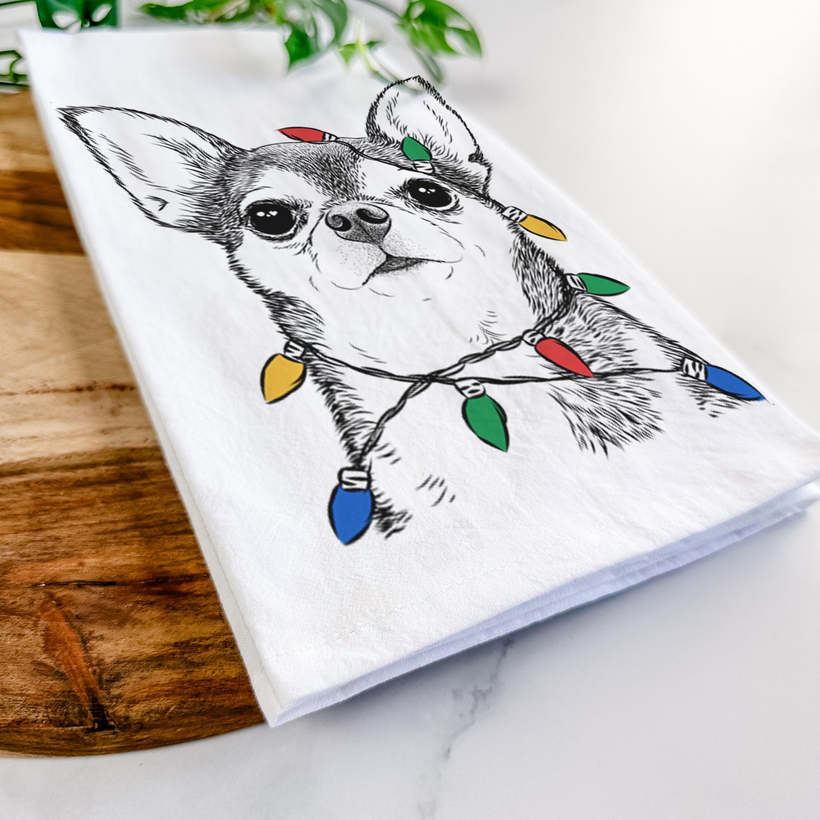 Hand-drawn sketch of Baby the Chihuahua wrapped in Christmas lights on a tea towel