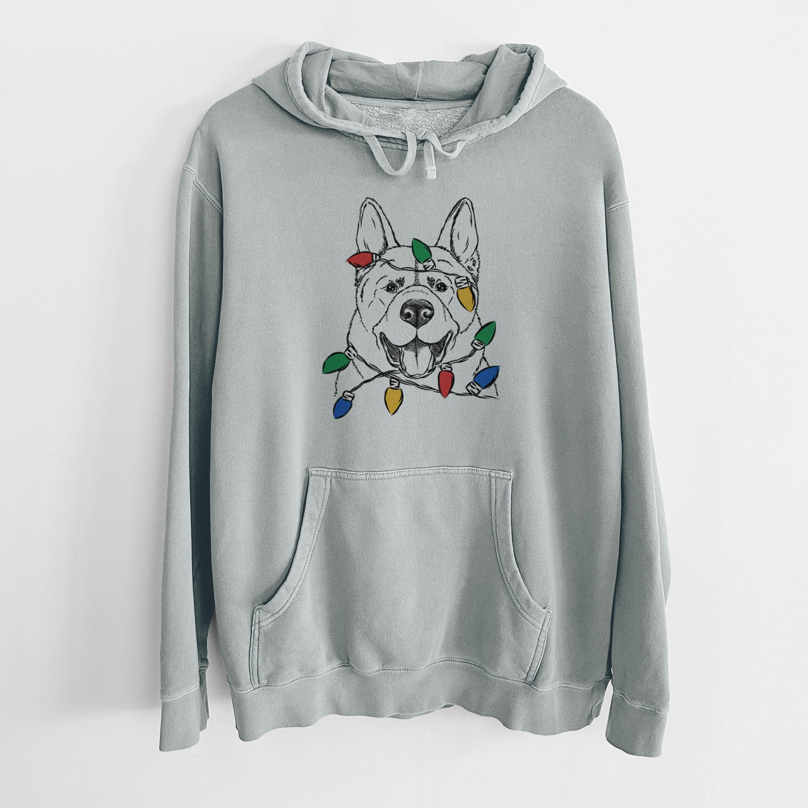 Hand-drawn sketch of Baku the Akita wrapped in Christmas lights on a Sage Unisex pigment dyed hoodie