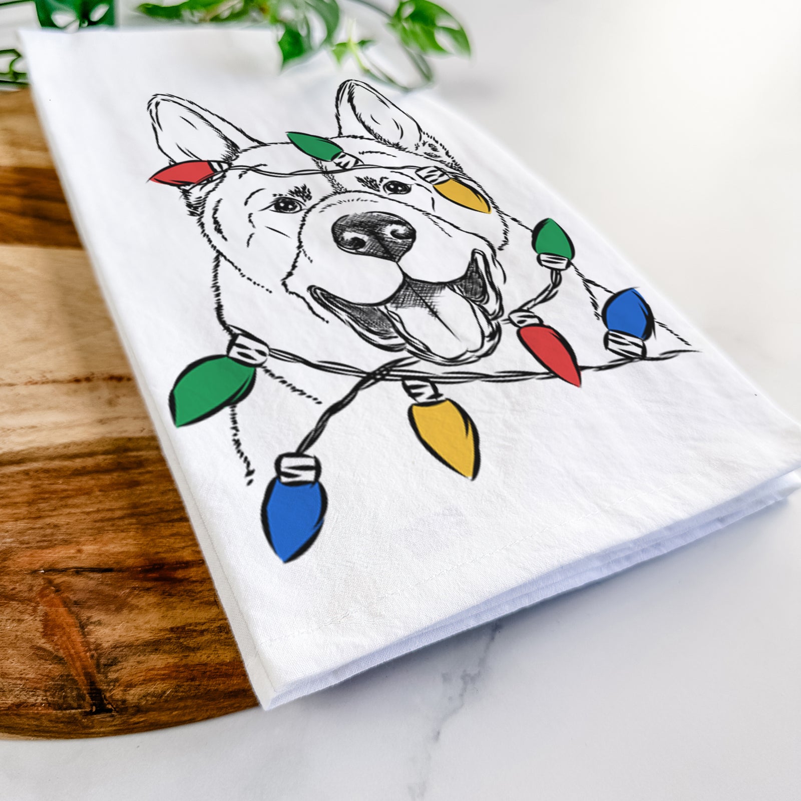 Hand-drawn sketch of Baku the Akita wrapped in Christmas lights on a tea towel