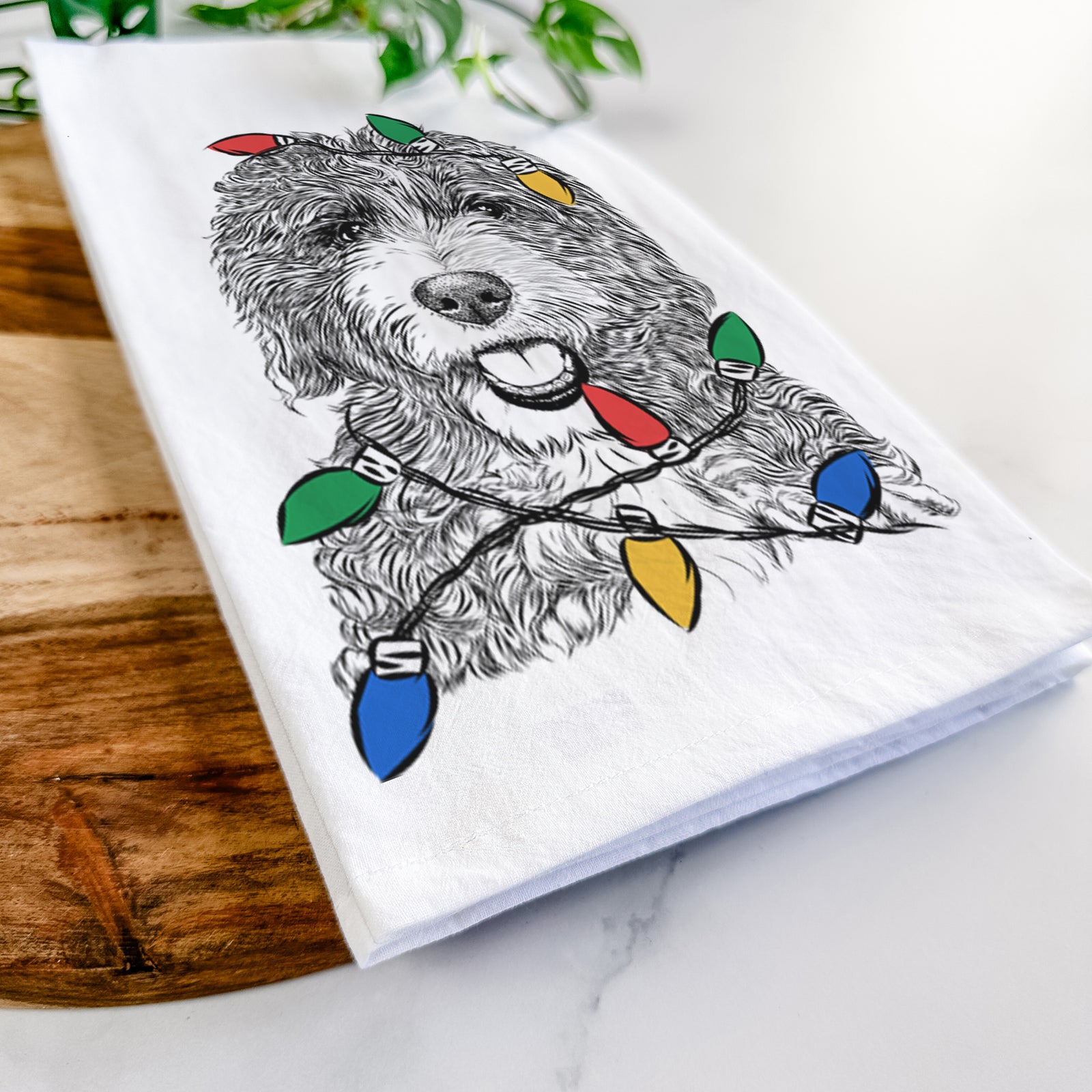Hand-drawn sketch of Bash the Bernedoodle wrapped in Christmas lights on a tea towel
