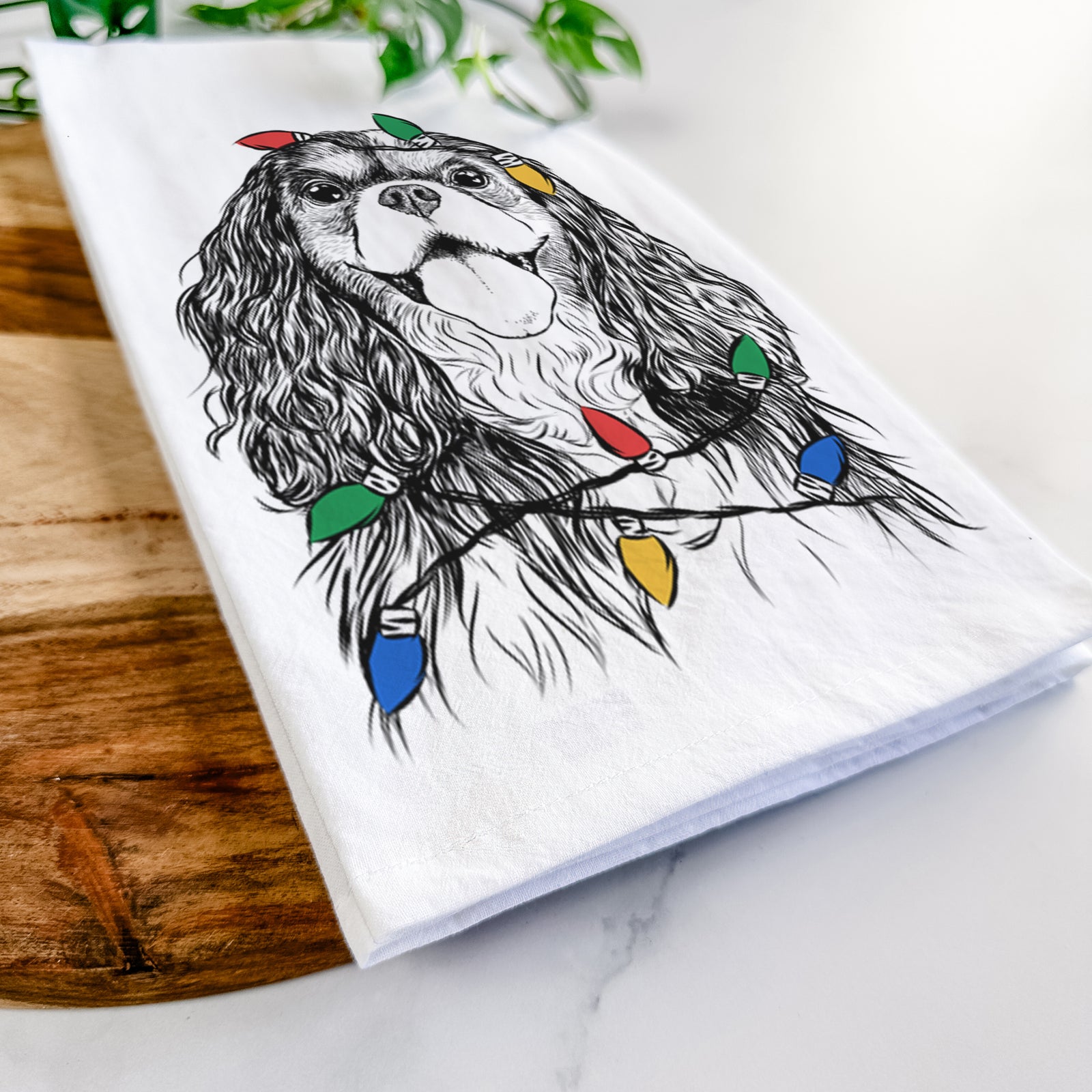 Hand-drawn sketch of Brandy the Cavalier King Charles Spaniel wrapped in Christmas lights on a tea towel