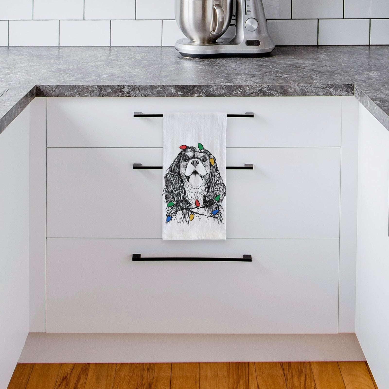 Hand-drawn sketch of Brandy the Cavalier King Charles Spaniel wrapped in Christmas lights on a tea towel, hanging on an oven door in a kitchen