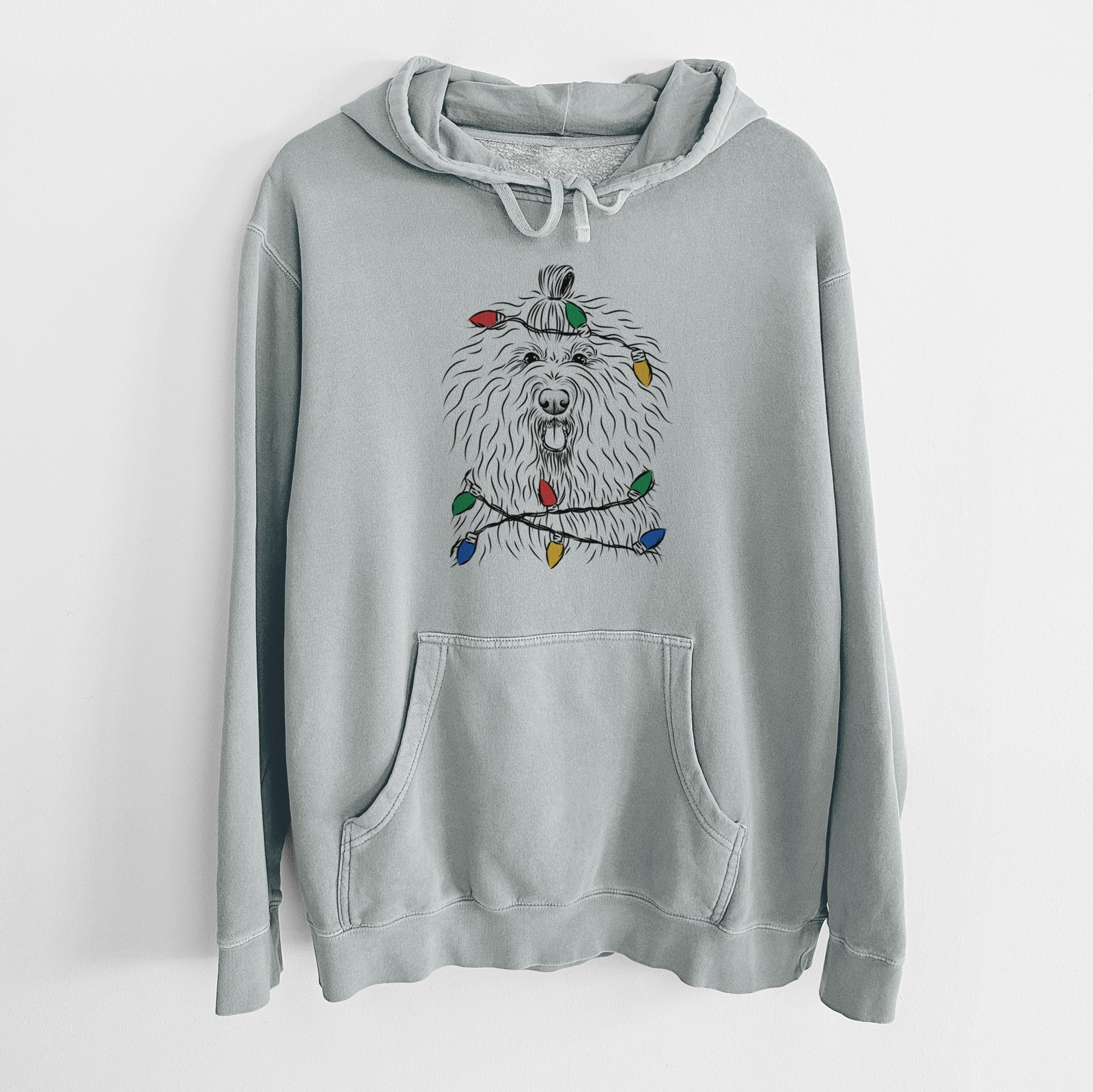 Hand-drawn sketch of Brody the Old English Sheepdog wrapped in Christmas lights on a Sage Unisex pigment dyed hoodie