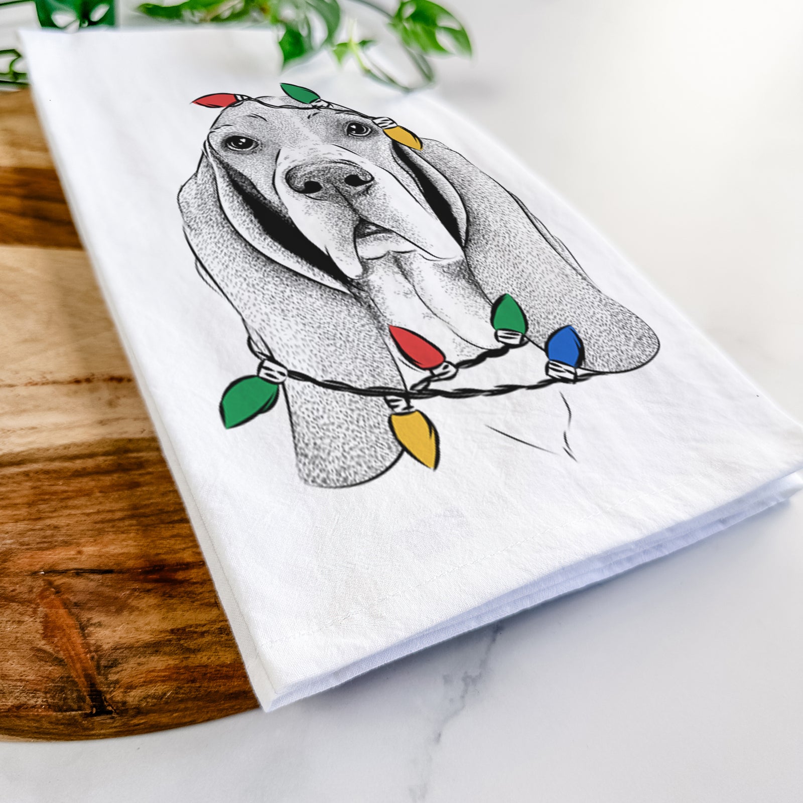 Hand-drawn sketch of Buckley the Basset Hound wrapped in Christmas lights on a tea towel
