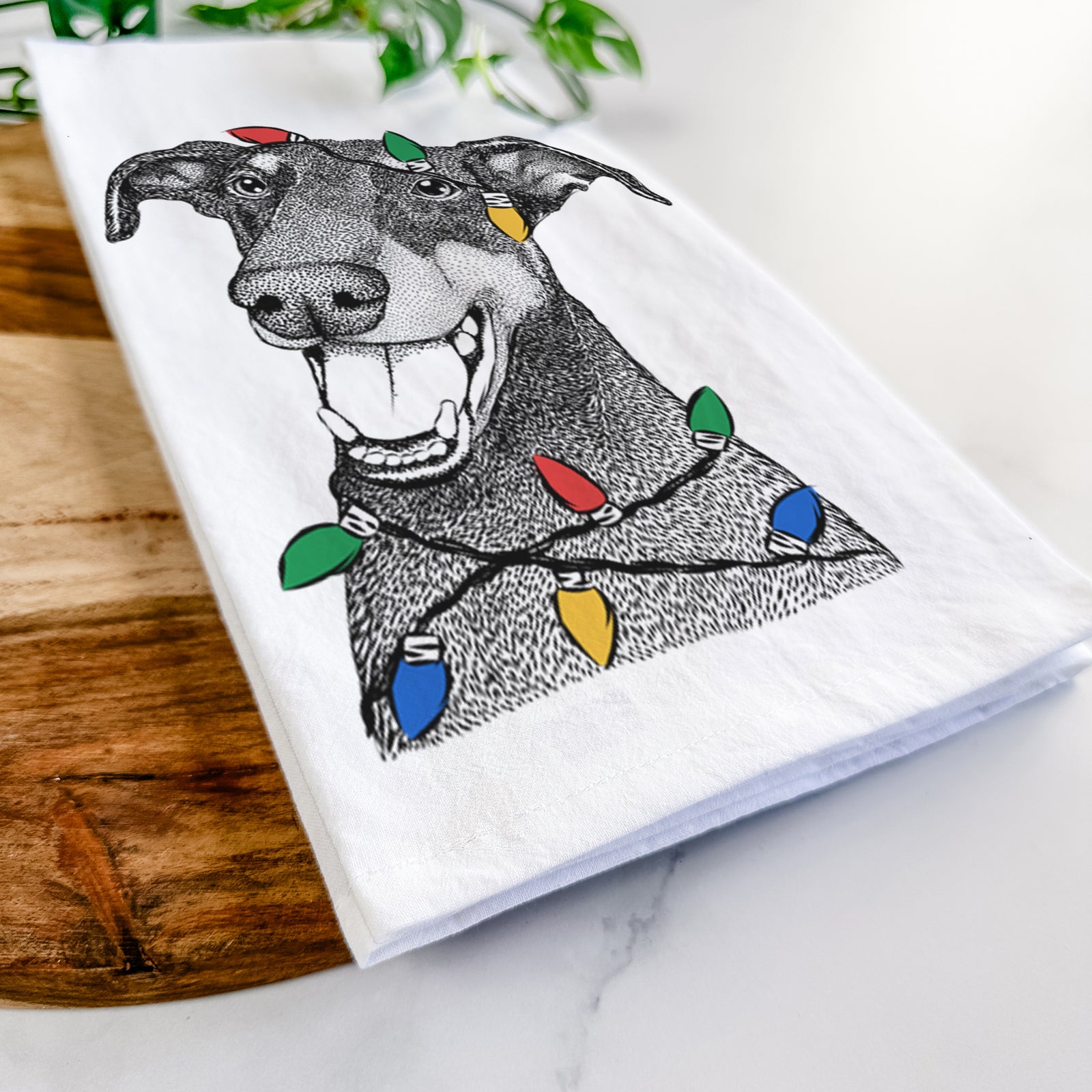 Hand-drawn sketch of Bunnie the Doberman Pinscher wrapped in Christmas lights on a tea towel