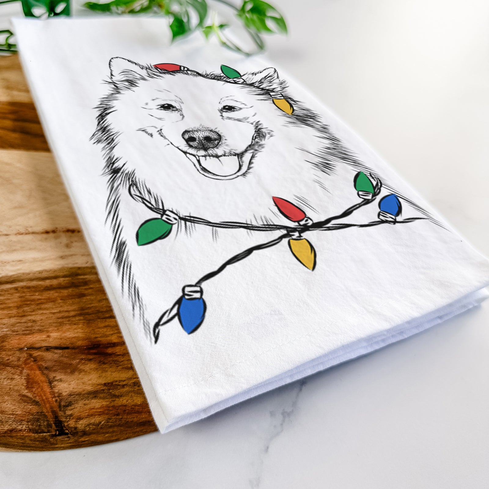 Hand-drawn sketch of Caico the Samoyed wrapped in Christmas lights on a tea towel