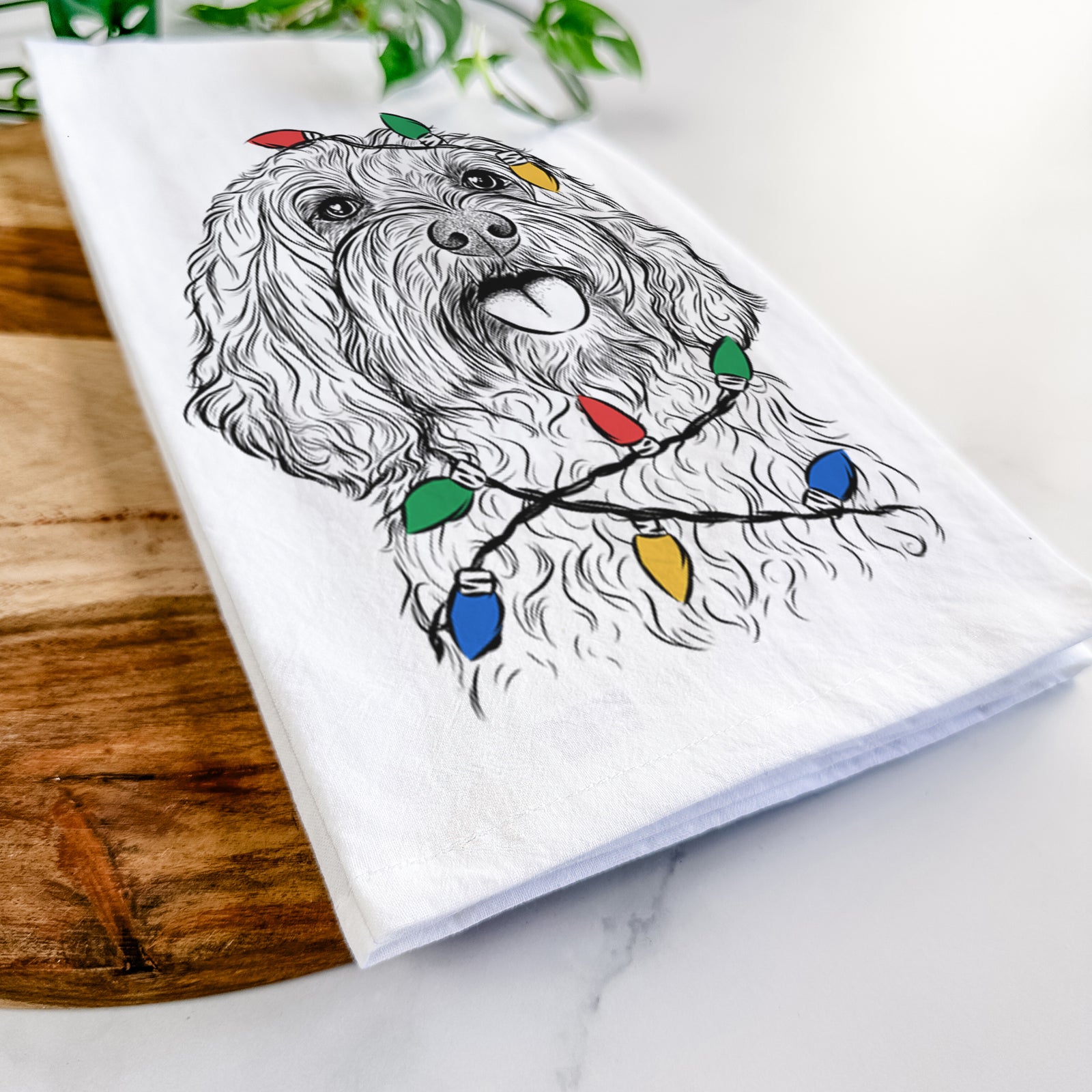Hand-drawn sketch of Cali the Cavapoo wrapped in Christmas lights on a tea towel