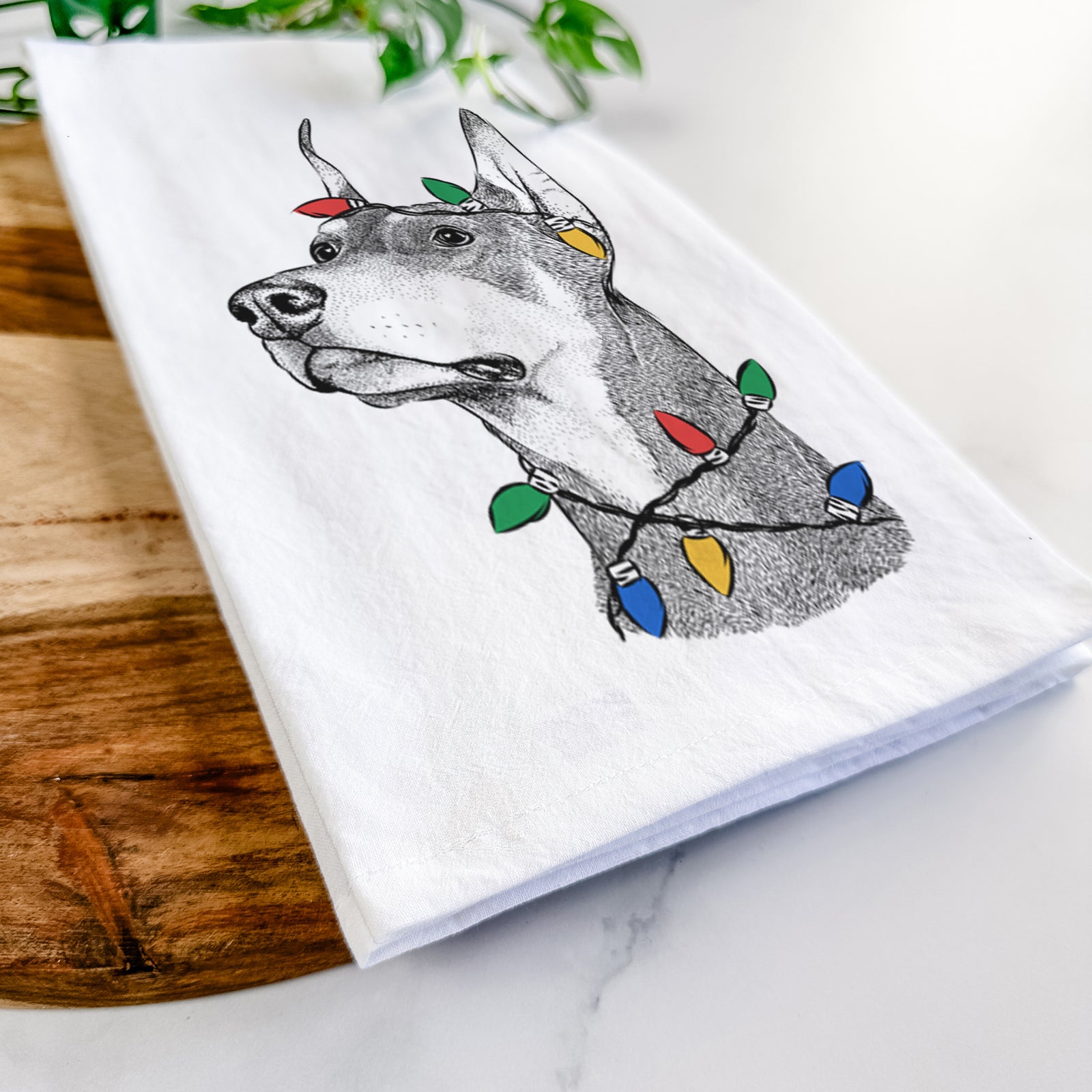 Hand-drawn sketch of Cenza the Doberman Pinscher wrapped in Christmas lights on a tea towel