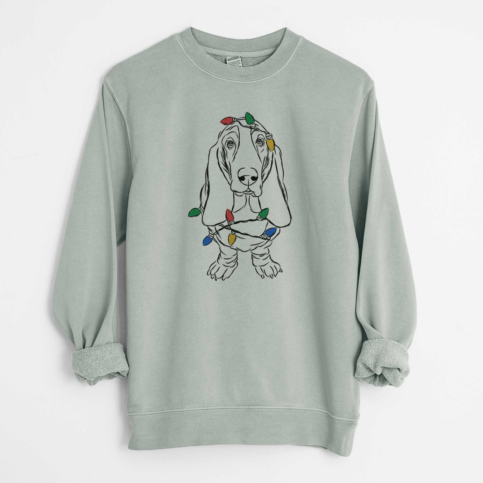 Hand-drawn sketch of Charlie the Basset Hound wrapped in Christmas lights on a Sage Unisex pigment dyed crew sweatshirt