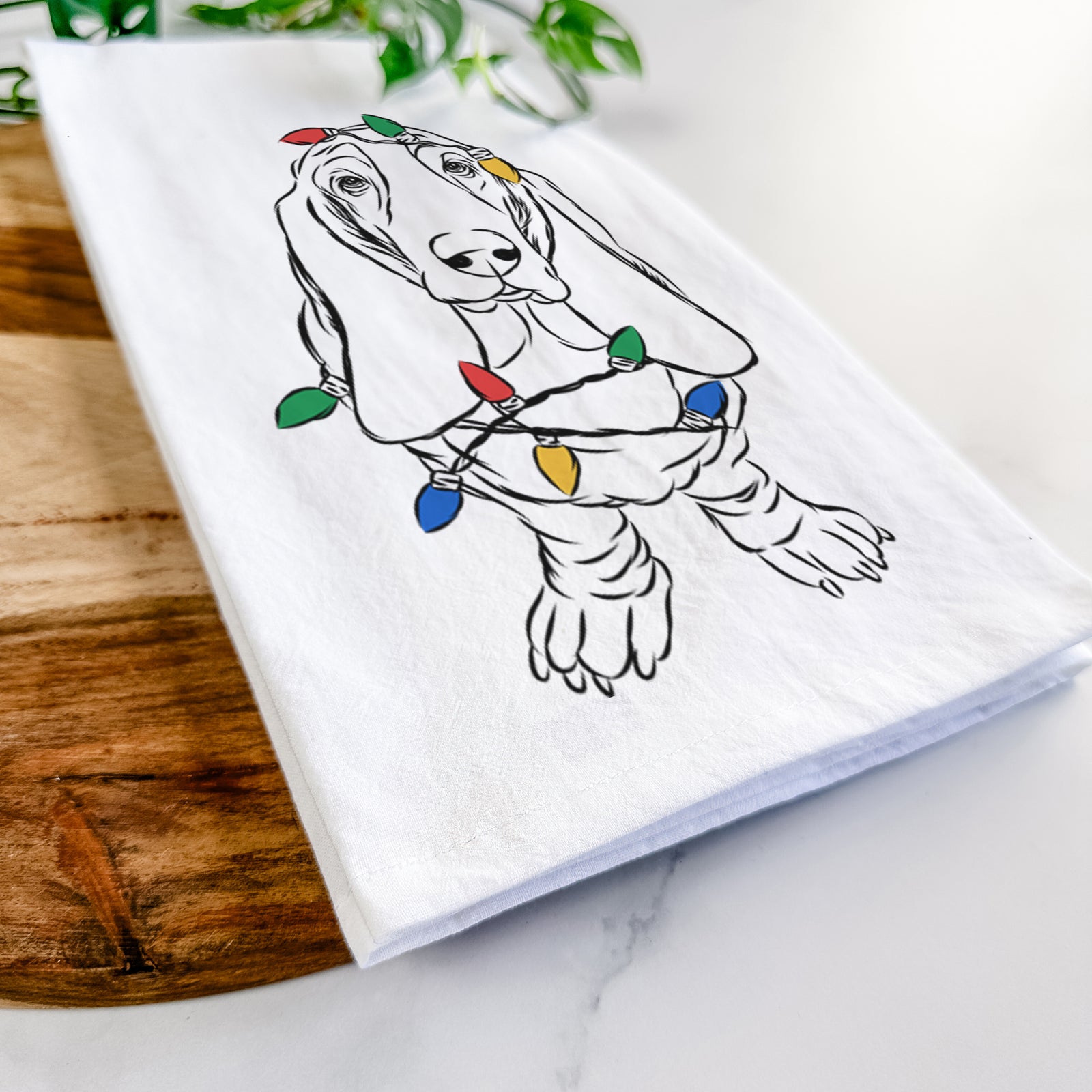 Hand-drawn sketch of Charlie the Basset Hound wrapped in Christmas lights on a tea towel