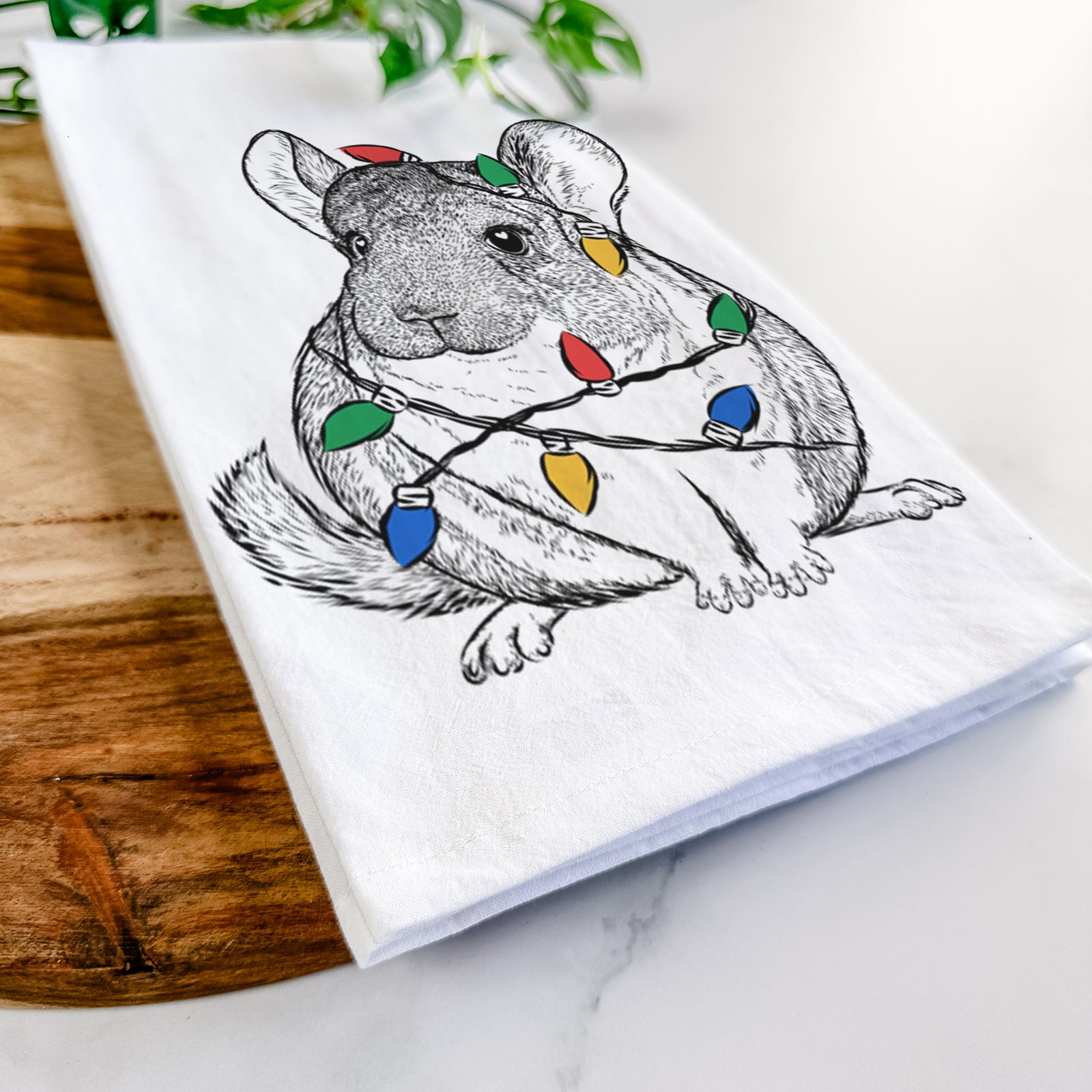 Hand-drawn sketch of Cheddar the Chinchilla wrapped in Christmas lights on a tea towel