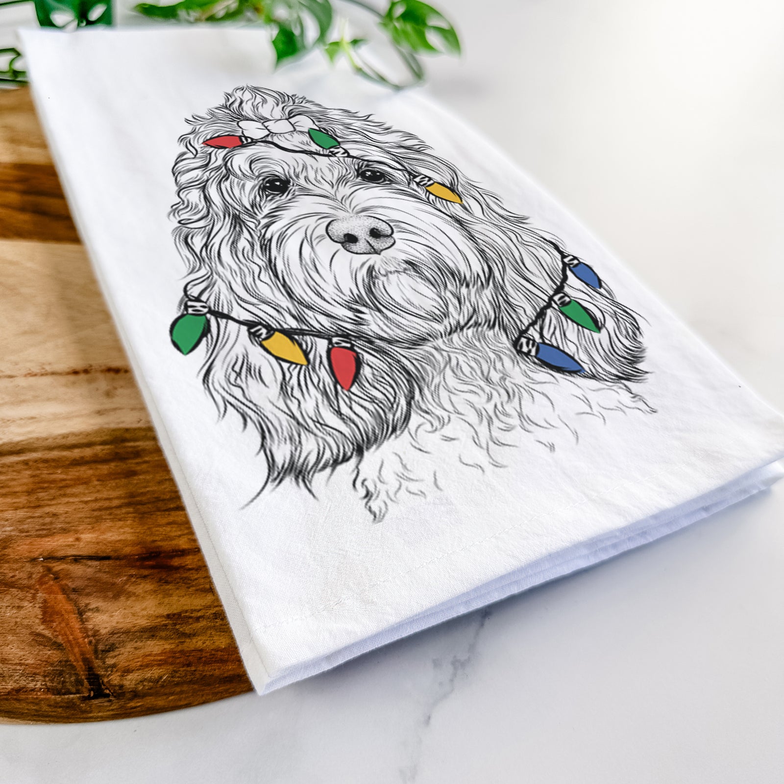 Hand-drawn sketch of Chloe the Cockapoo wrapped in Christmas lights on a tea towel