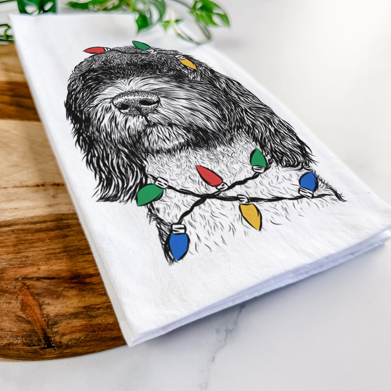 Hand-drawn sketch of Chris the Portuguese Water Dog wrapped in Christmas lights on a tea towel