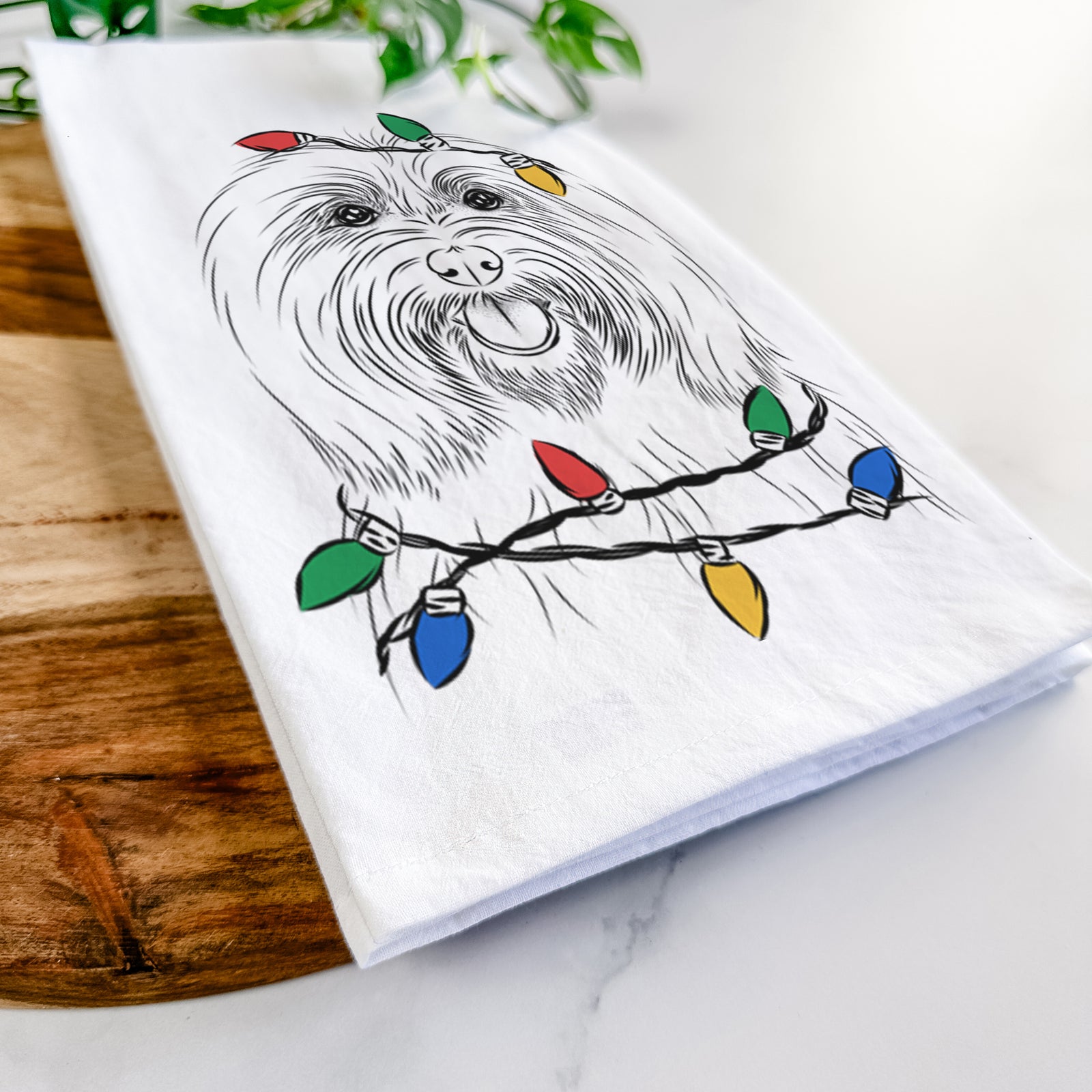 Hand-drawn sketch of Claude the Coton de Tulear wrapped in Christmas lights on a tea towel