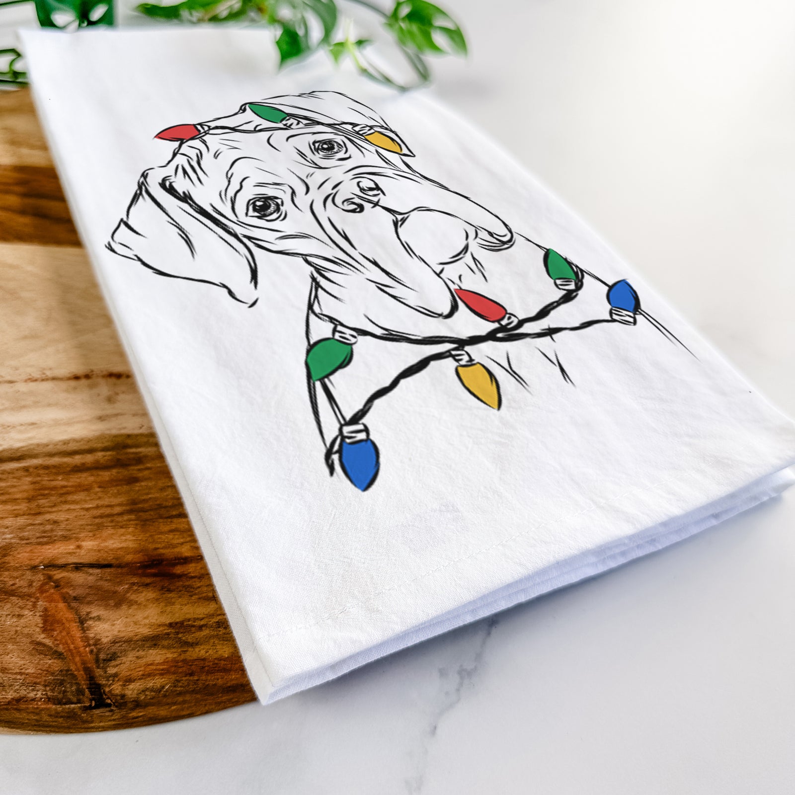 Hand-drawn sketch of Cooper the Boxer wrapped in Christmas lights on a tea towel