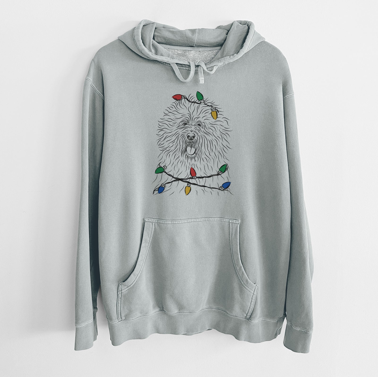 Hand-drawn sketch of Cozie the Old English Sheepdog wrapped in Christmas lights on a Sage Unisex pigment dyed hoodie