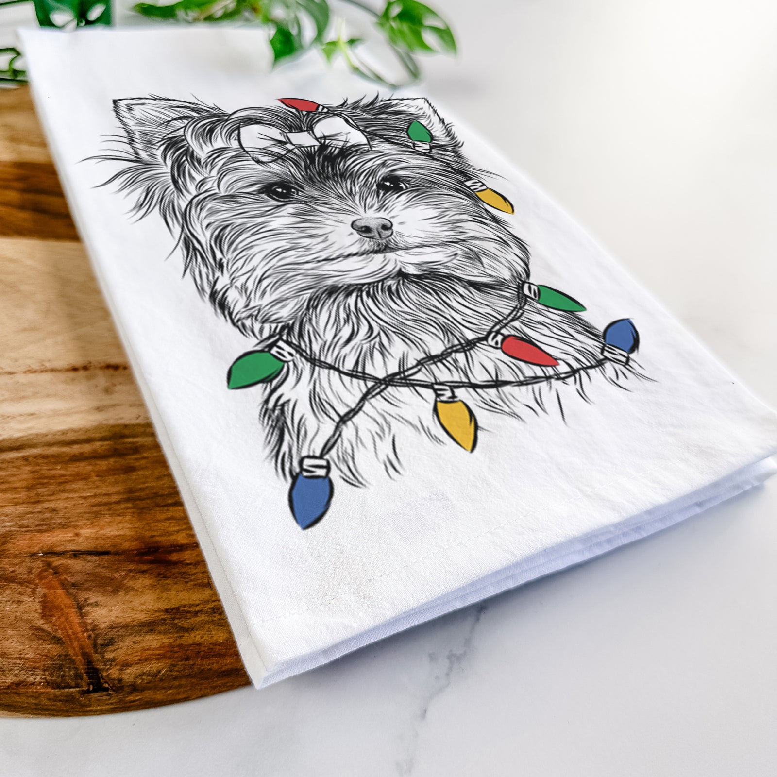 Hand-drawn sketch of Cricket the Biewer Terrier wrapped in Christmas lights on a tea towel