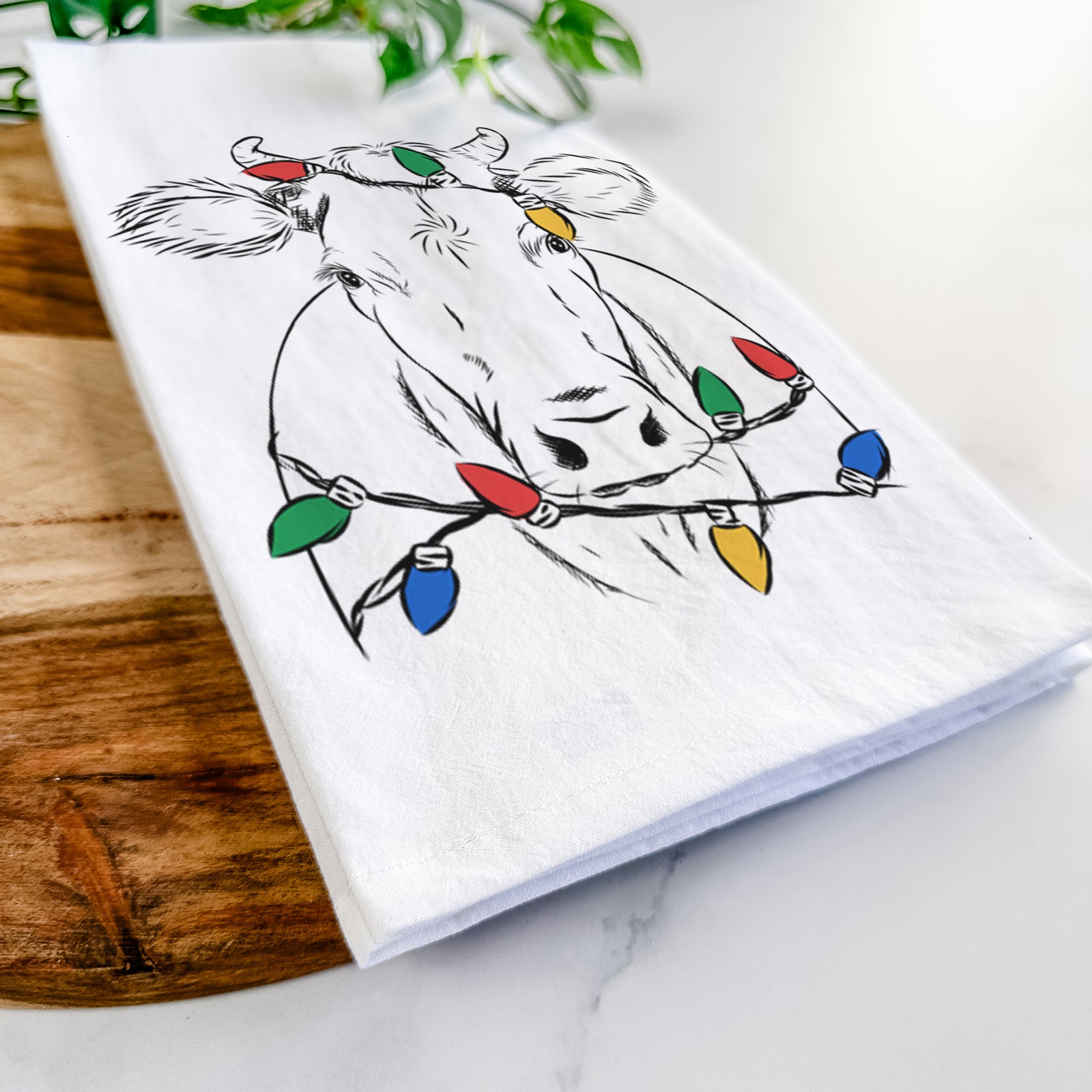 Hand-drawn sketch of Cruz the Cow wrapped in Christmas lights on a tea towel