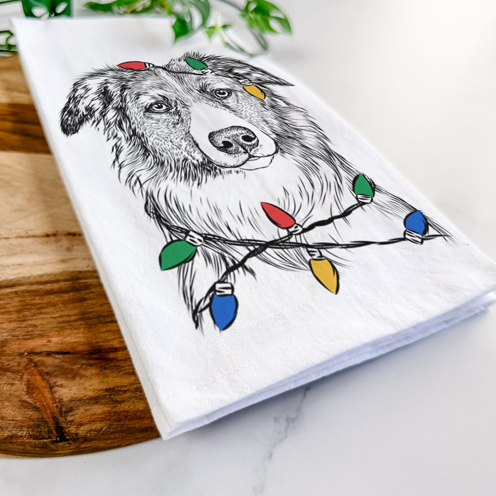 Hand-drawn sketch of Cynder the English Shepherd wrapped in Christmas lights on a tea towel