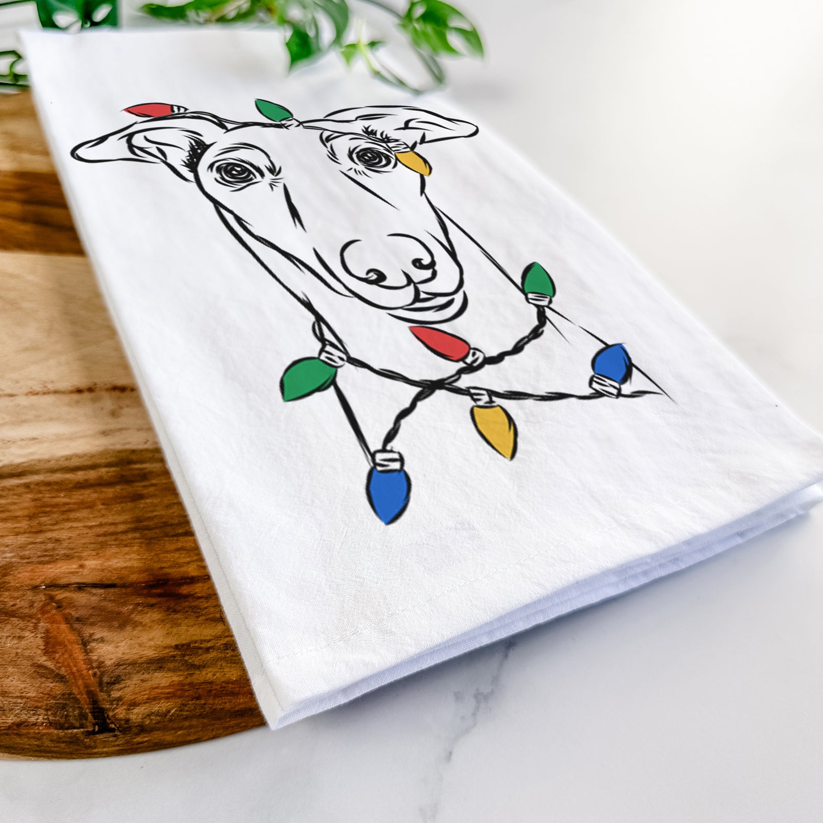 Hand-drawn sketch of Diva the Greyhound wrapped in Christmas lights on a tea towel