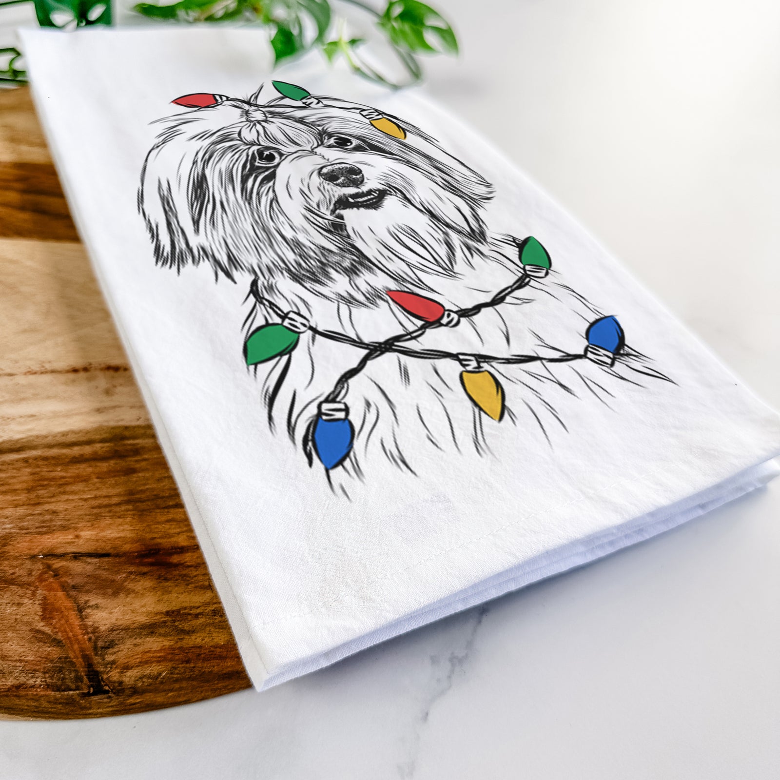 Hand-drawn sketch of Dooley the Havanese wrapped in Christmas lights on a tea towel