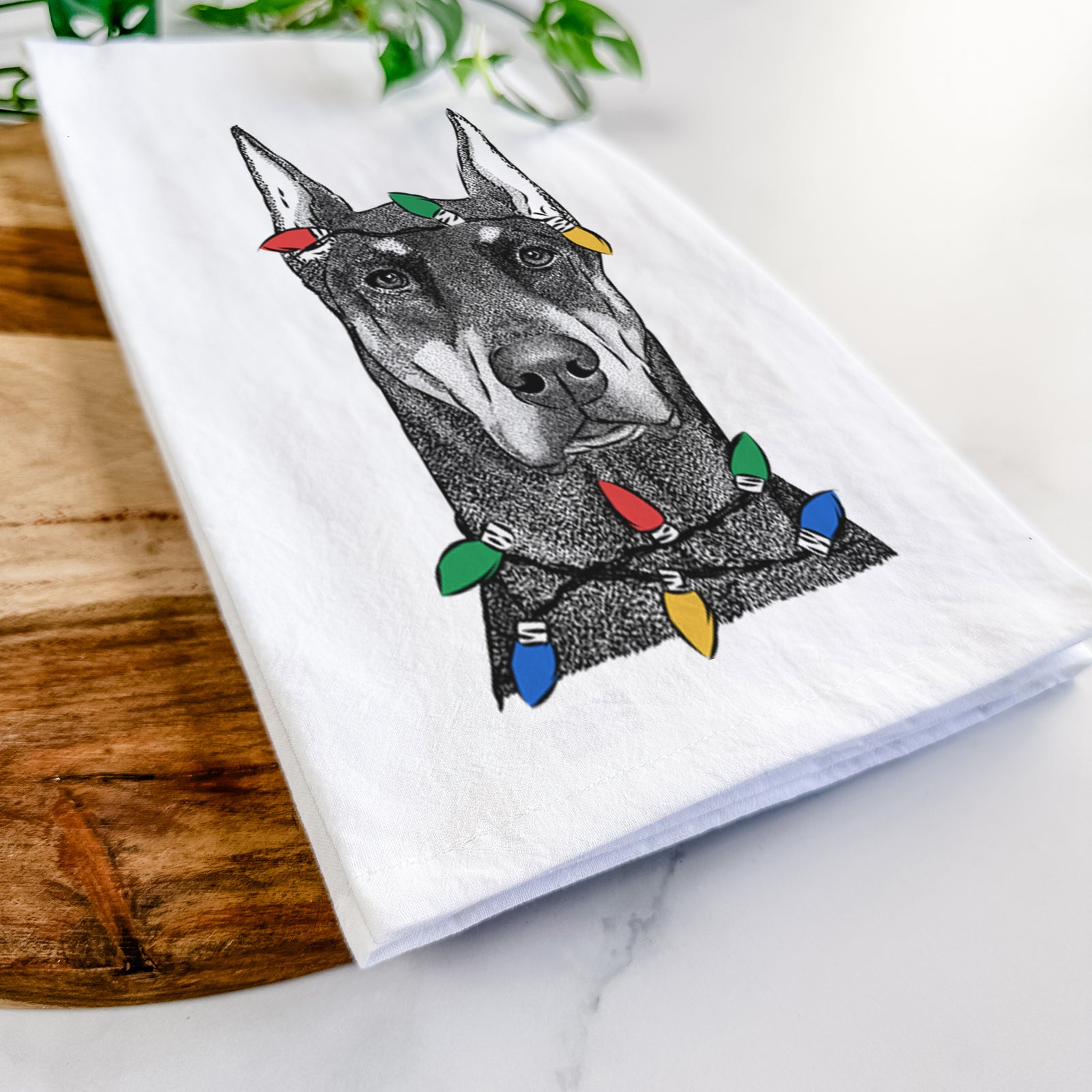 Hand-drawn sketch of Drake the Doberman Pinscher wrapped in Christmas lights on a tea towel