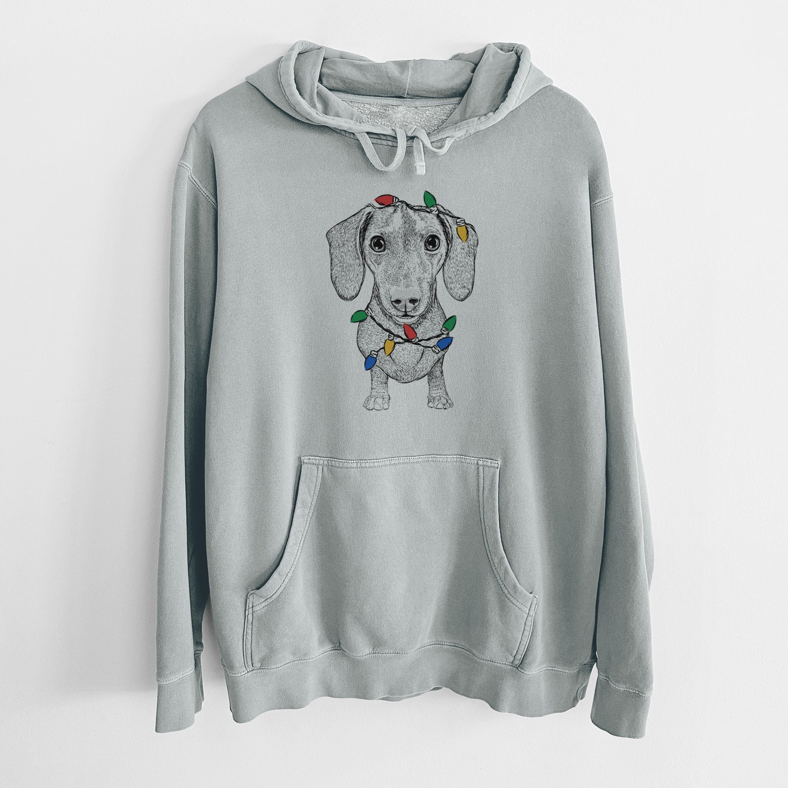 Hand-drawn sketch of Ernie the Mini Dachshund wrapped in Christmas lights on a Sage Unisex pigment dyed hoodie
