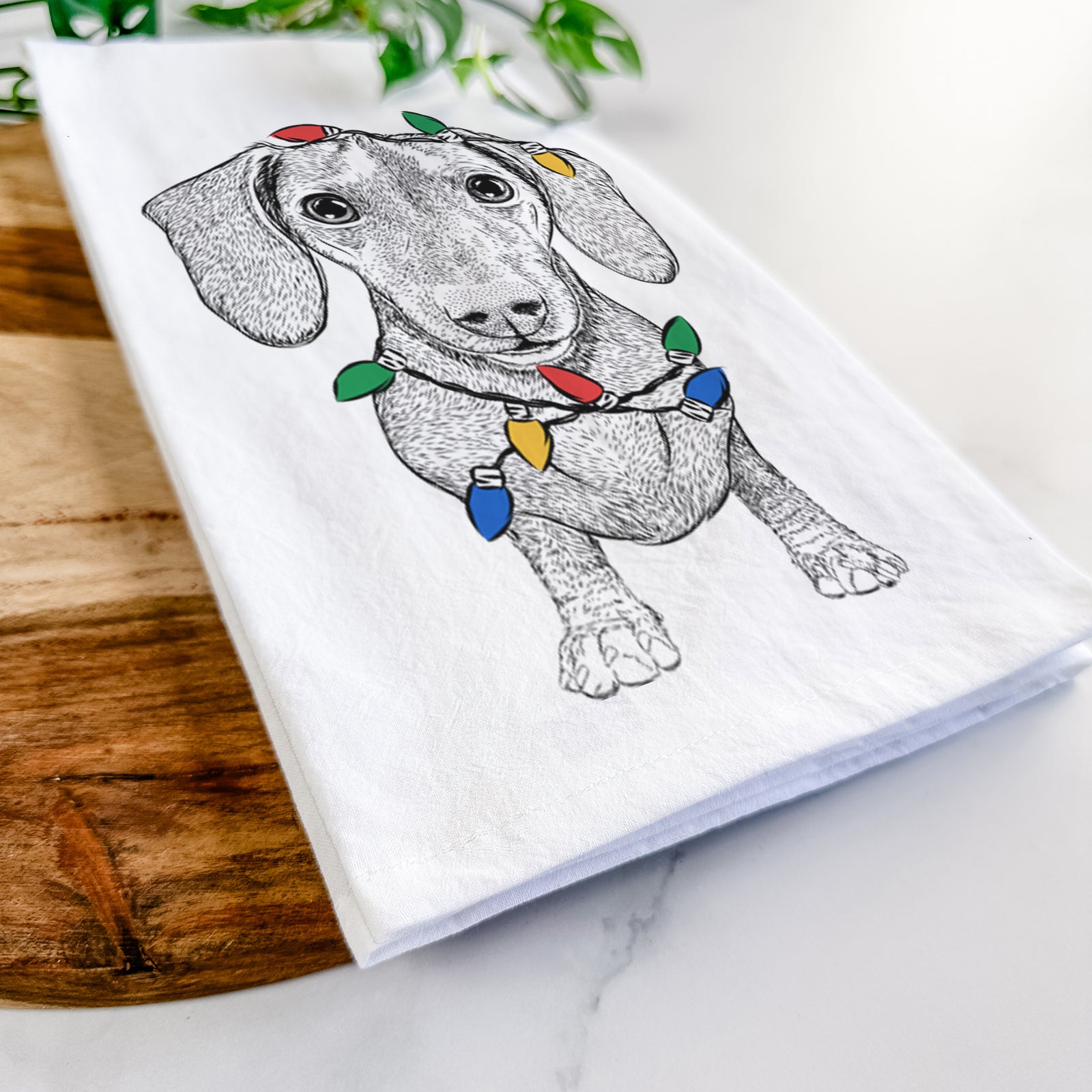 Hand-drawn sketch of Ernie the Mini Dachshund wrapped in Christmas lights on a tea towel