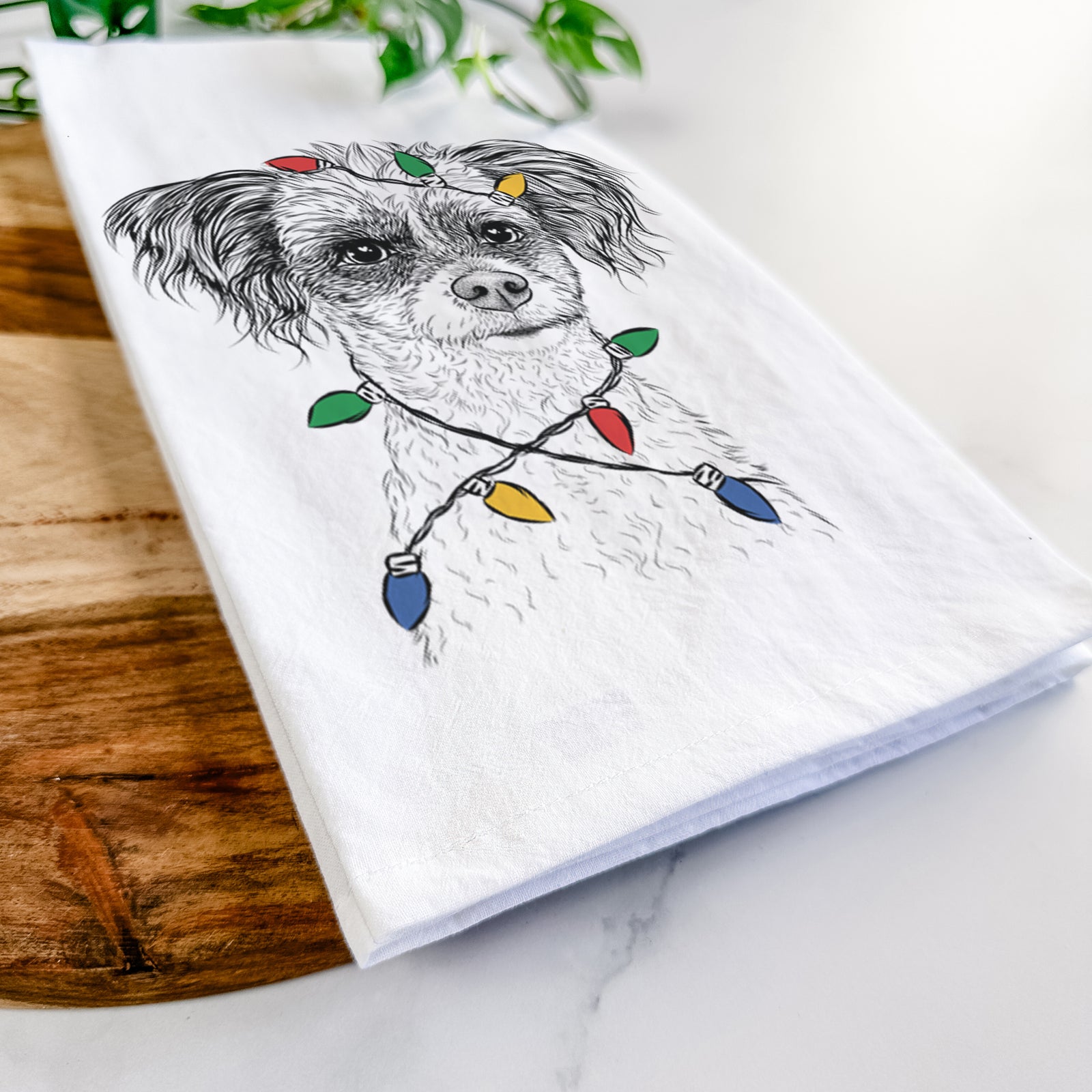 Hand-drawn sketch of Finley the Papillon Mix wrapped in Christmas lights on a tea towel
