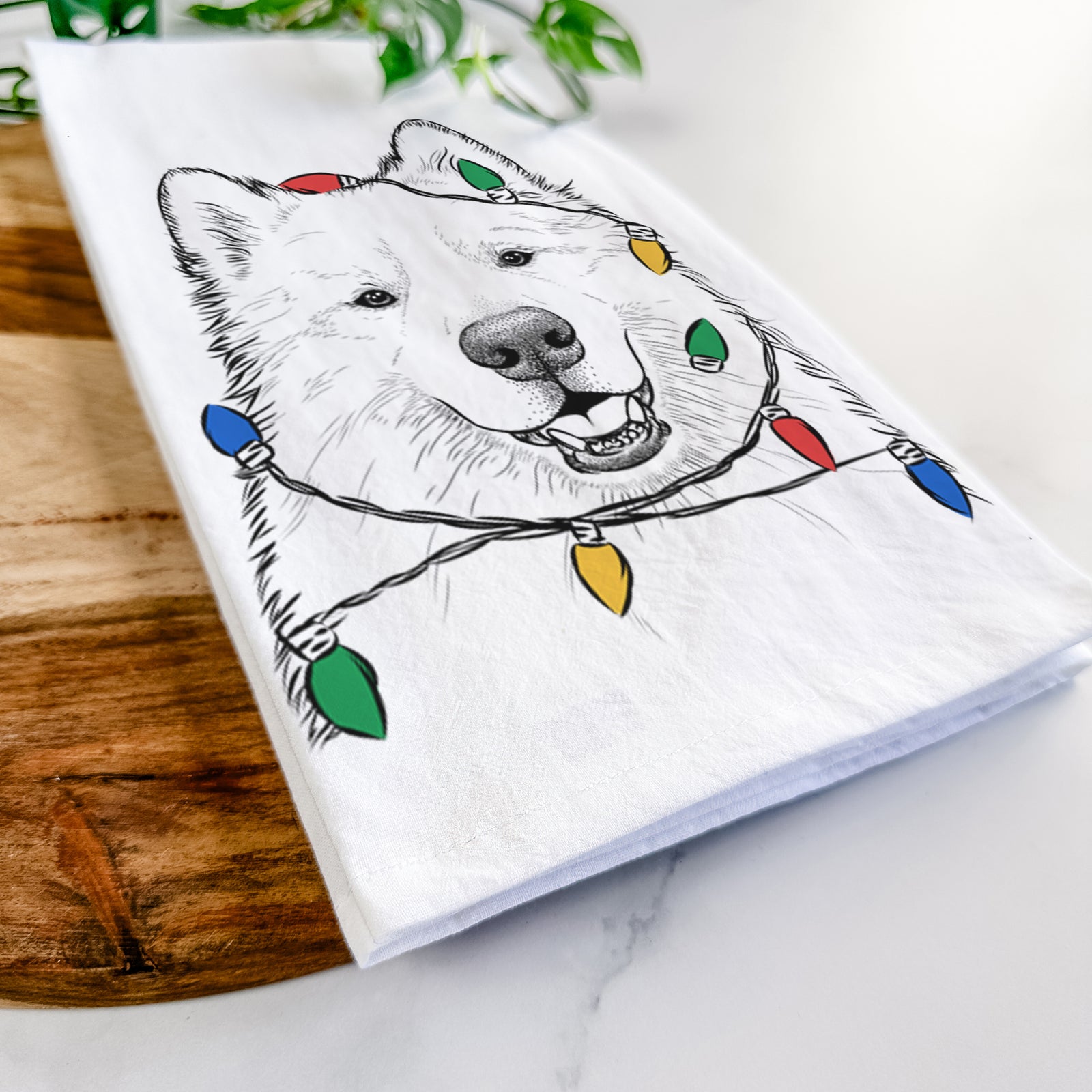 Hand-drawn sketch of Foster the Samoyed wrapped in Christmas lights on a tea towel