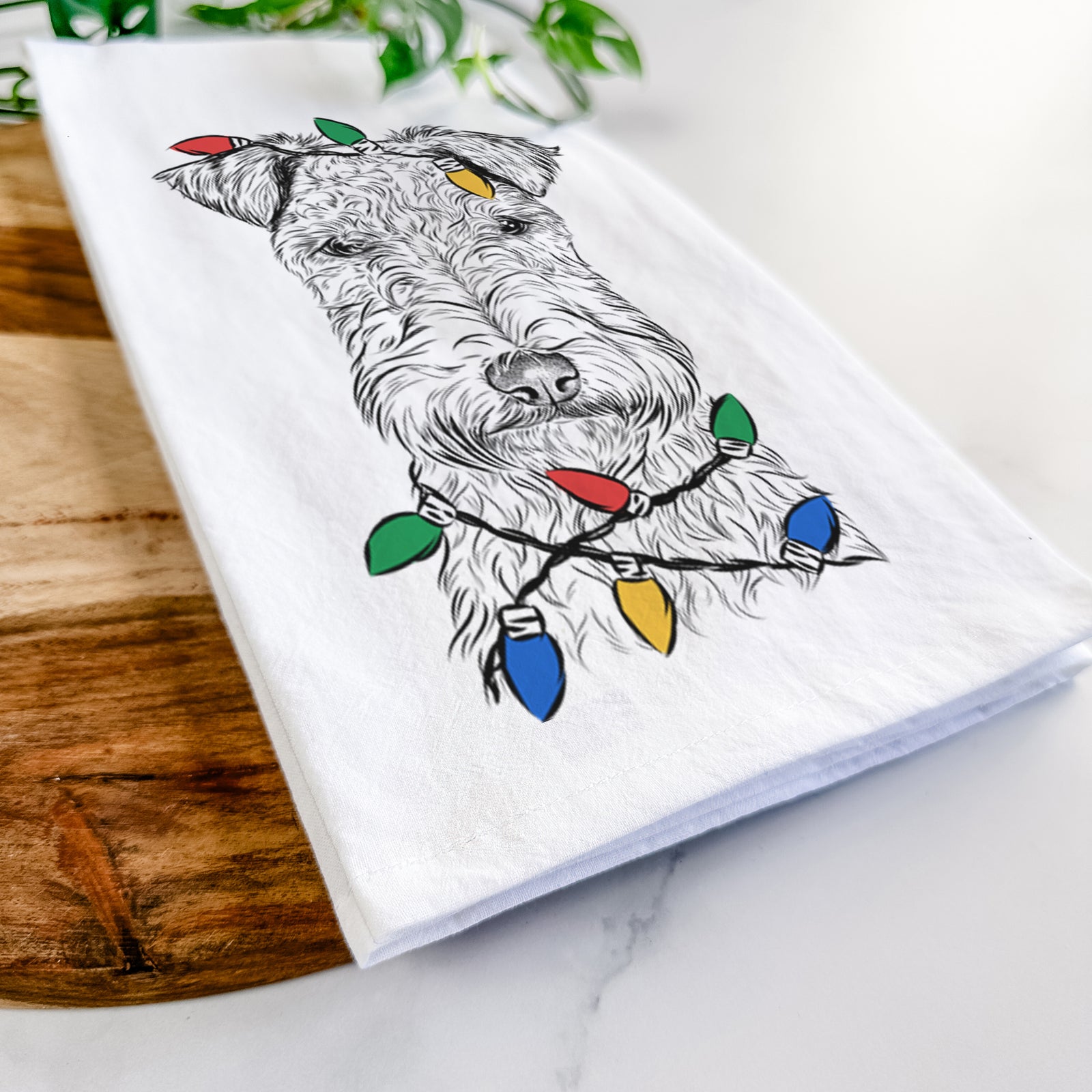 Hand-drawn sketch of Frida the Lakeland Terrier wrapped in Christmas lights on a tea towel