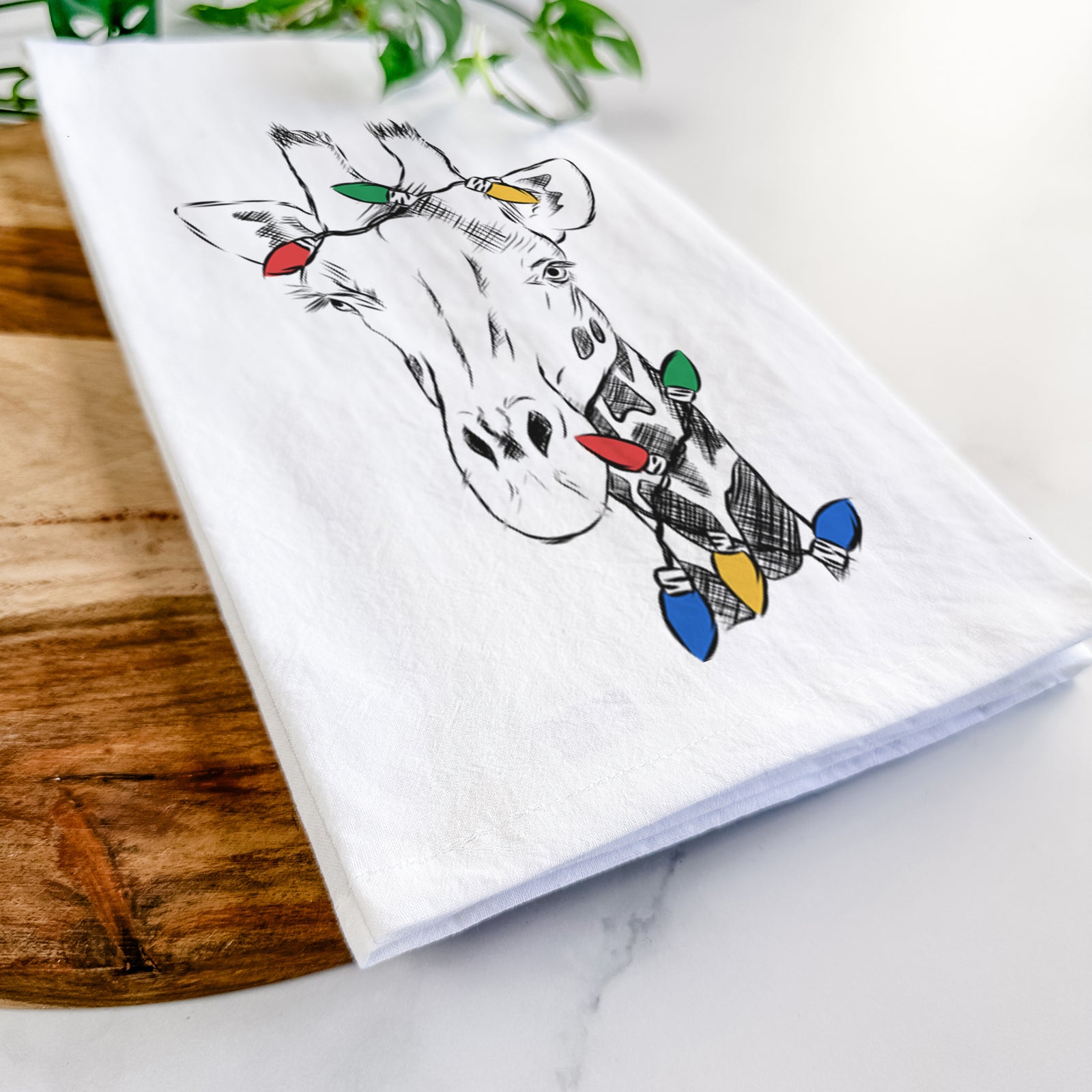 Hand-drawn sketch of Geoffrey the Giraffe wrapped in Christmas lights on a tea towel