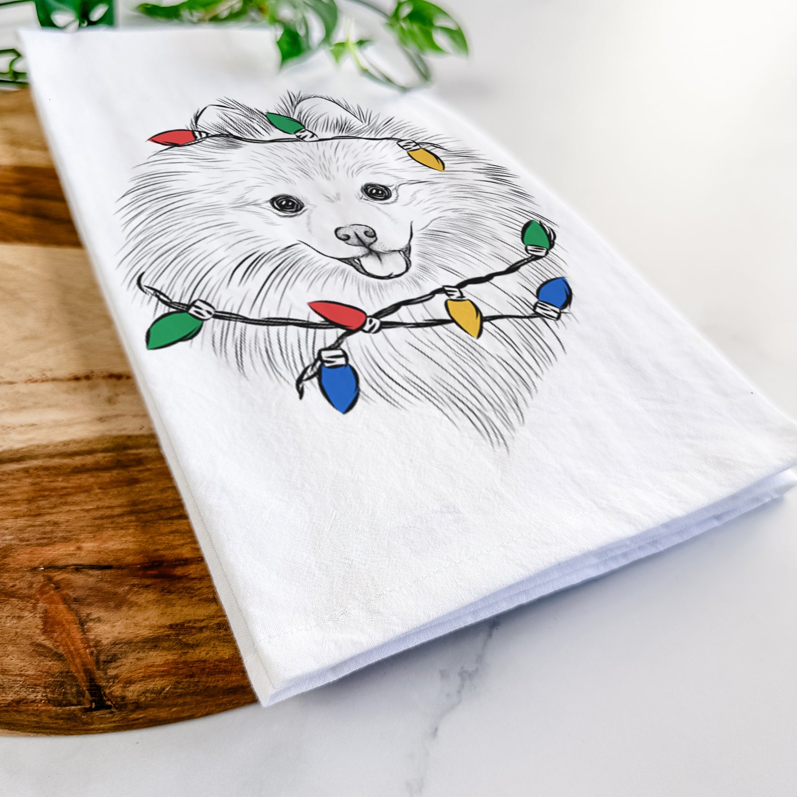 Hand-drawn sketch of GiGi the Pomeranian wrapped in Christmas lights on a tea towel