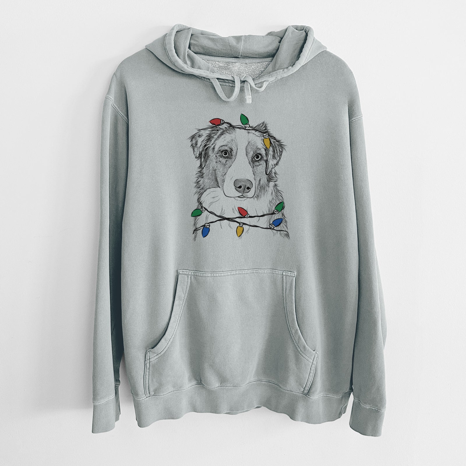 Hand-drawn sketch of Ginger the Australian Shepherd wrapped in Christmas lights on a Sage Unisex pigment dyed hoodie