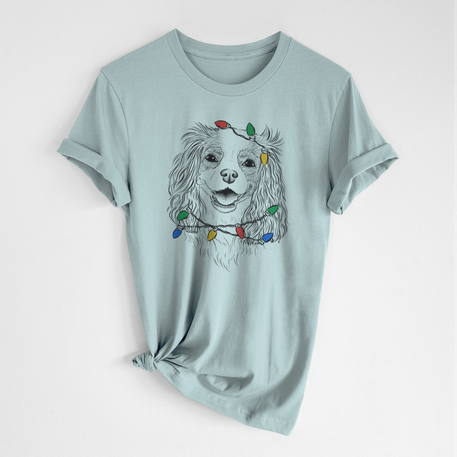 Hand-drawn sketch of Name the Cavalier King Charles Spaniel wrapped in Christmas lights on a Dusty Blue Unisex crewneck, worn by a woman