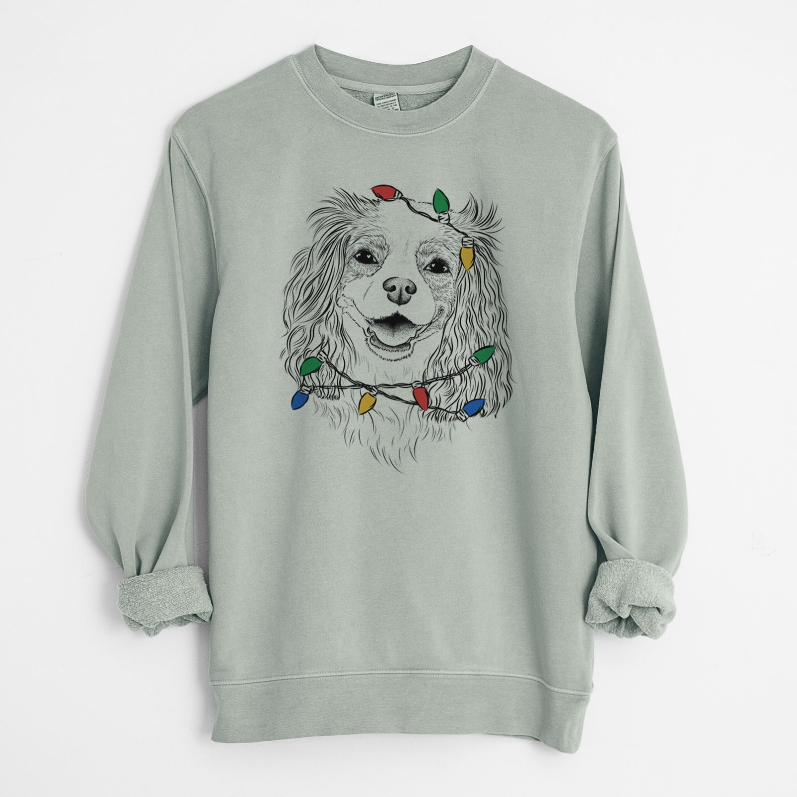 Hand-drawn sketch of Halley Comet the Cavalier King Charles Spaniel wrapped in Christmas lights on a Sage Unisex pigment dyed crew sweatshirt