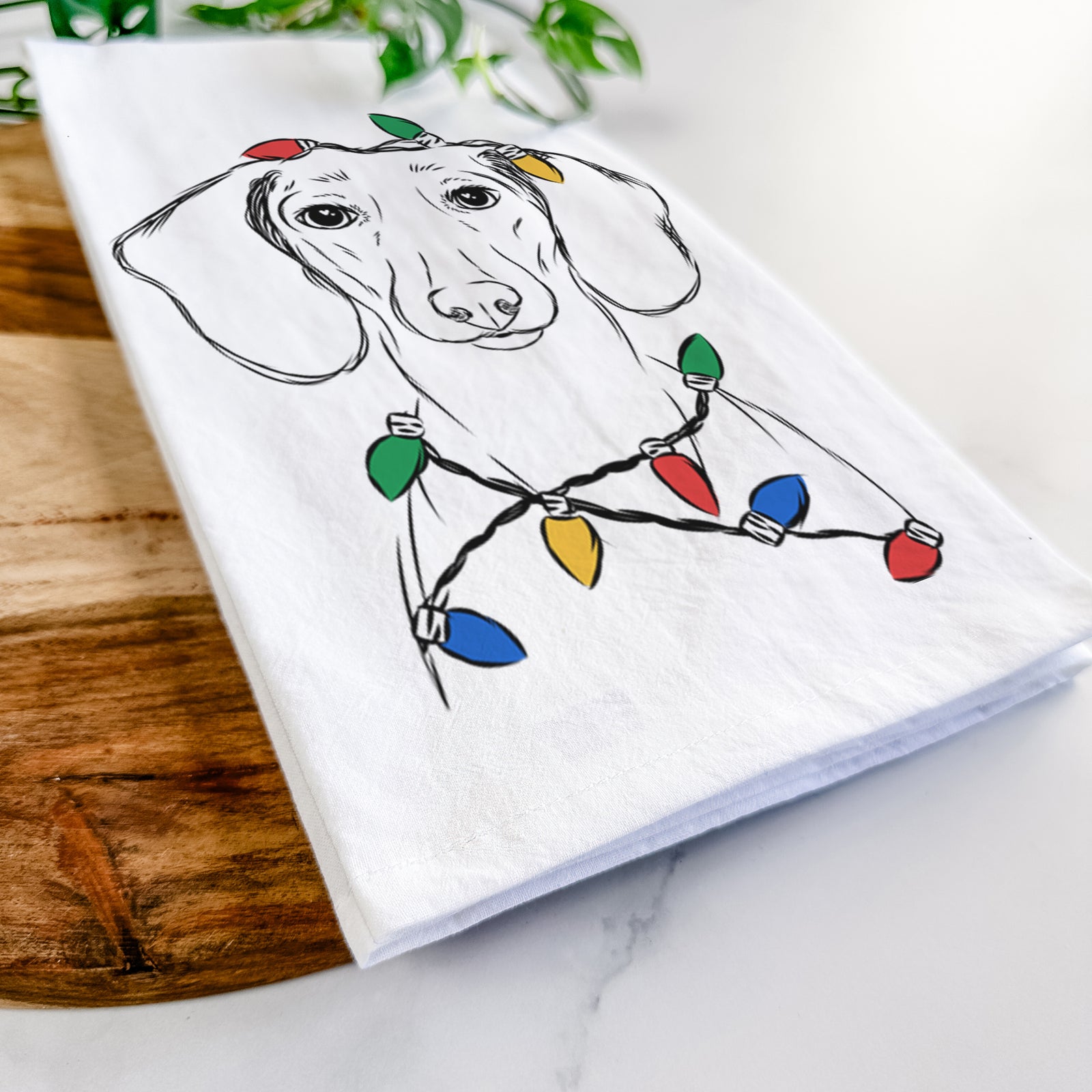 Hand-drawn sketch of Hans the Dachshund wrapped in Christmas lights on a tea towel