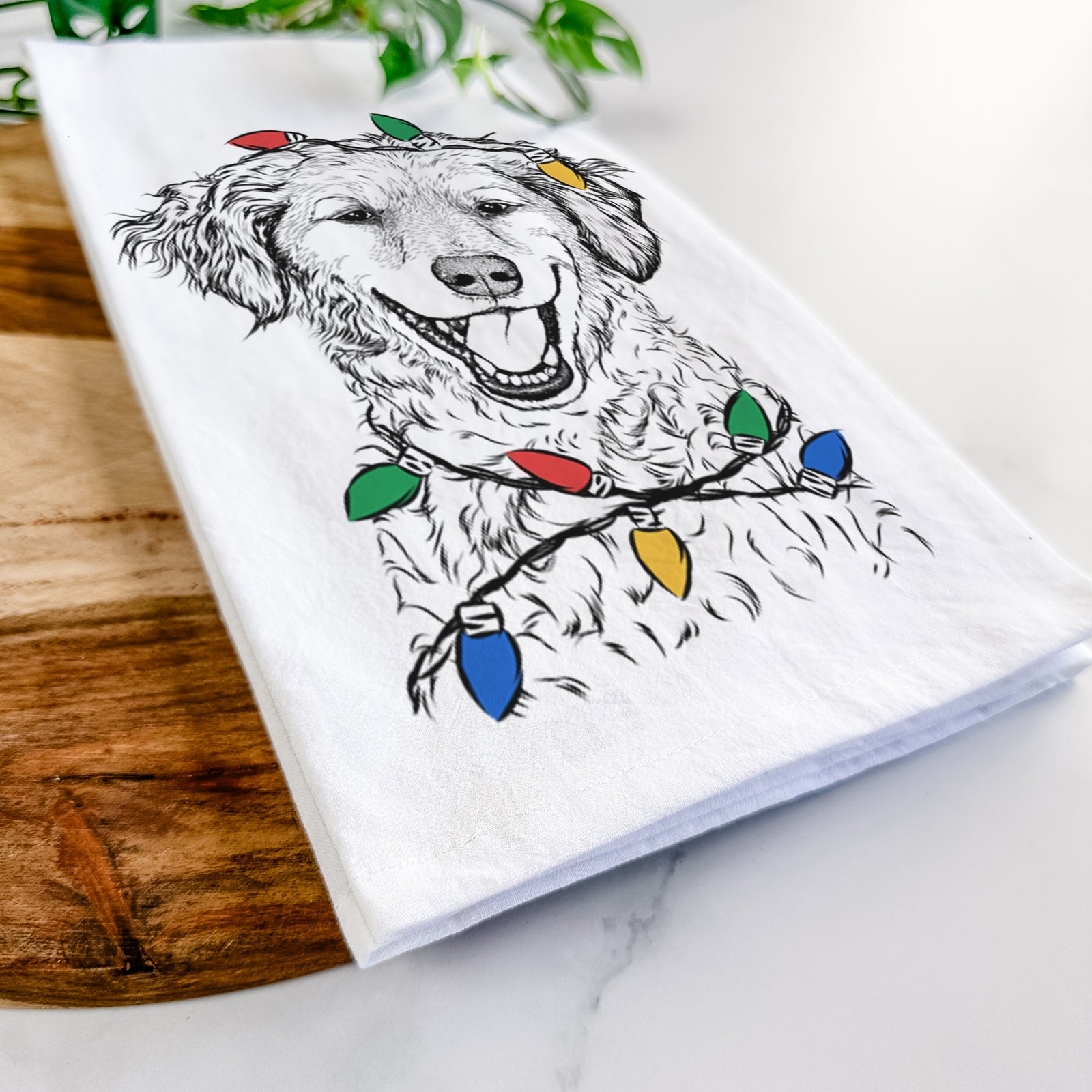 Hand-drawn sketch of Happy Otis the Miniature Goldendoodle wrapped in Christmas lights on a tea towel