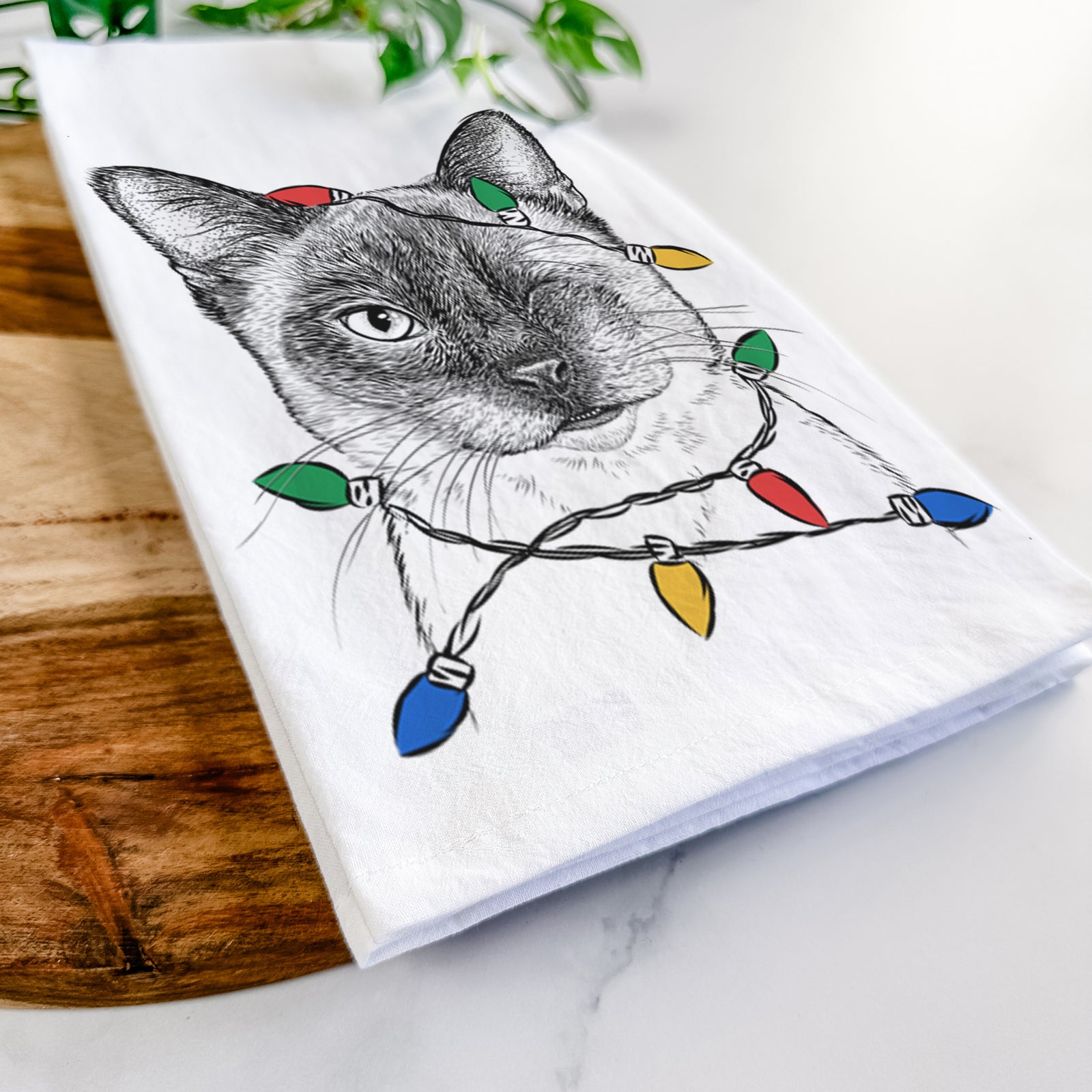 Hand-drawn sketch of Hoggle the Siamese Cat wrapped in Christmas lights on a tea towel