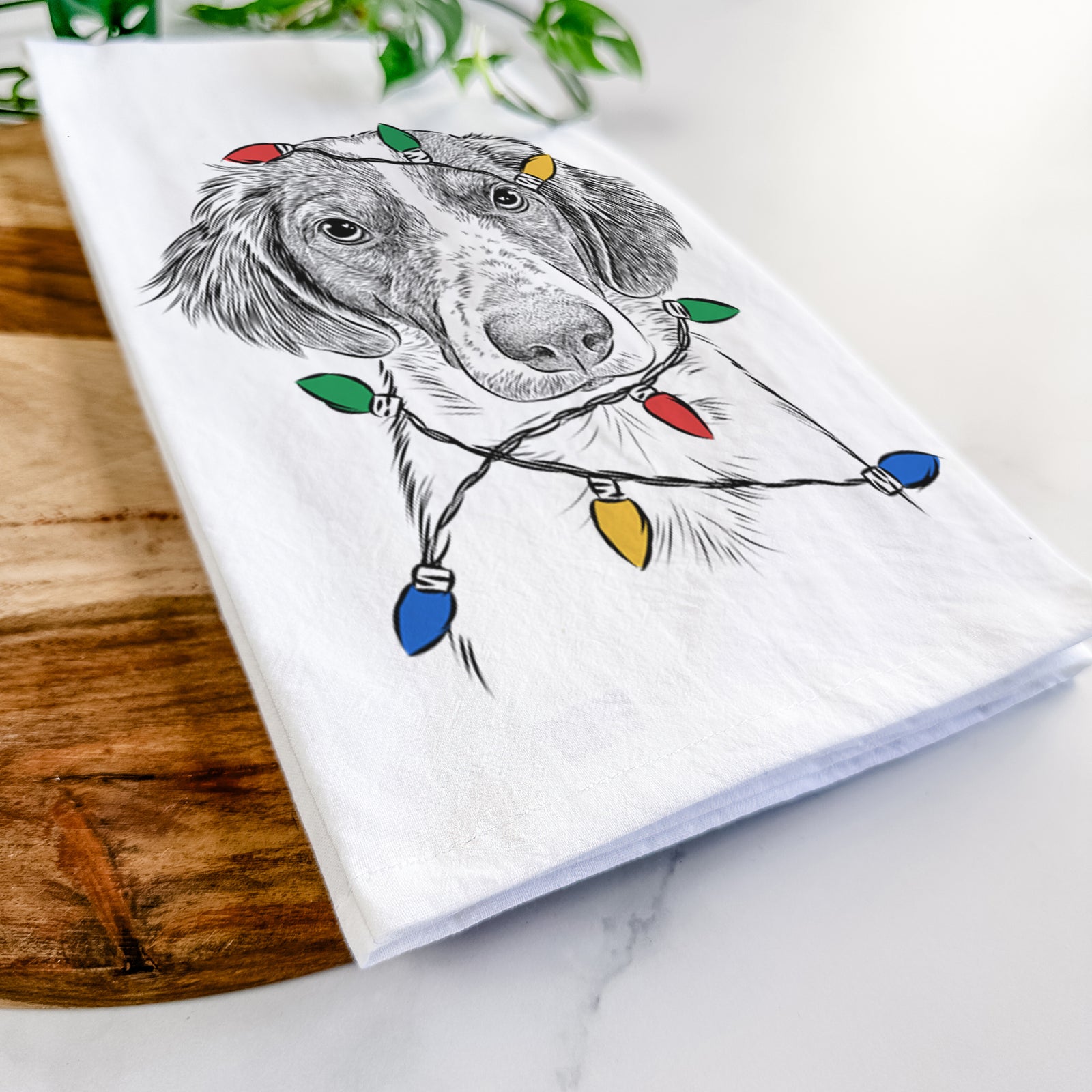 Hand-drawn sketch of Holly the Brittany Spaniel wrapped in Christmas lights on a tea towel