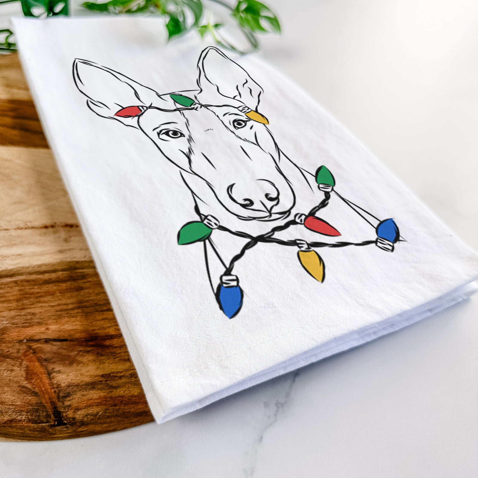Hand-drawn sketch of Indy the Ibizan Hound wrapped in Christmas lights on a tea towel