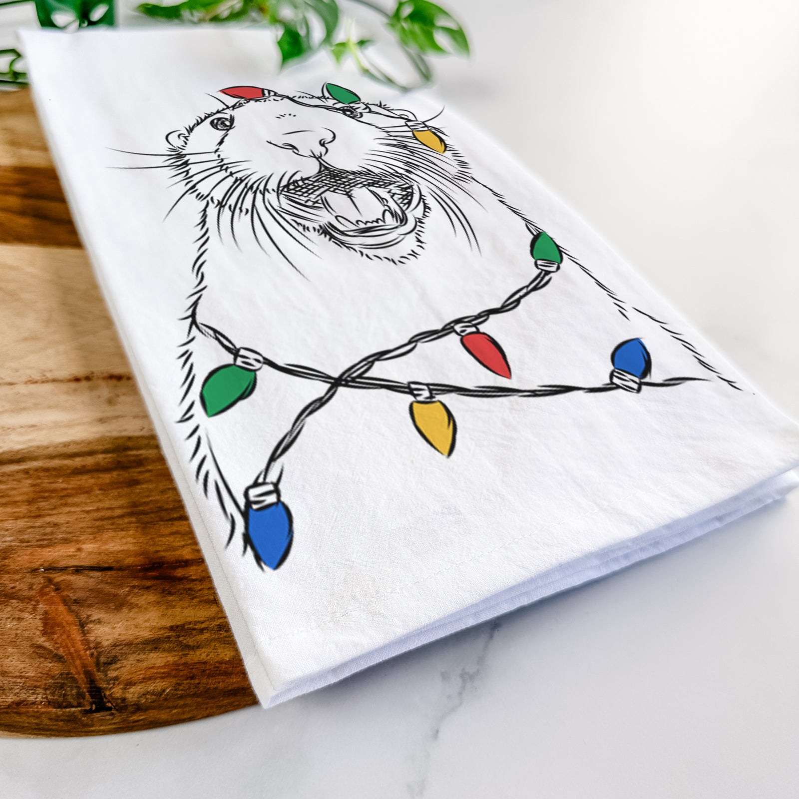 Hand-drawn sketch of Jasper the River Otter wrapped in Christmas lights on a tea towel