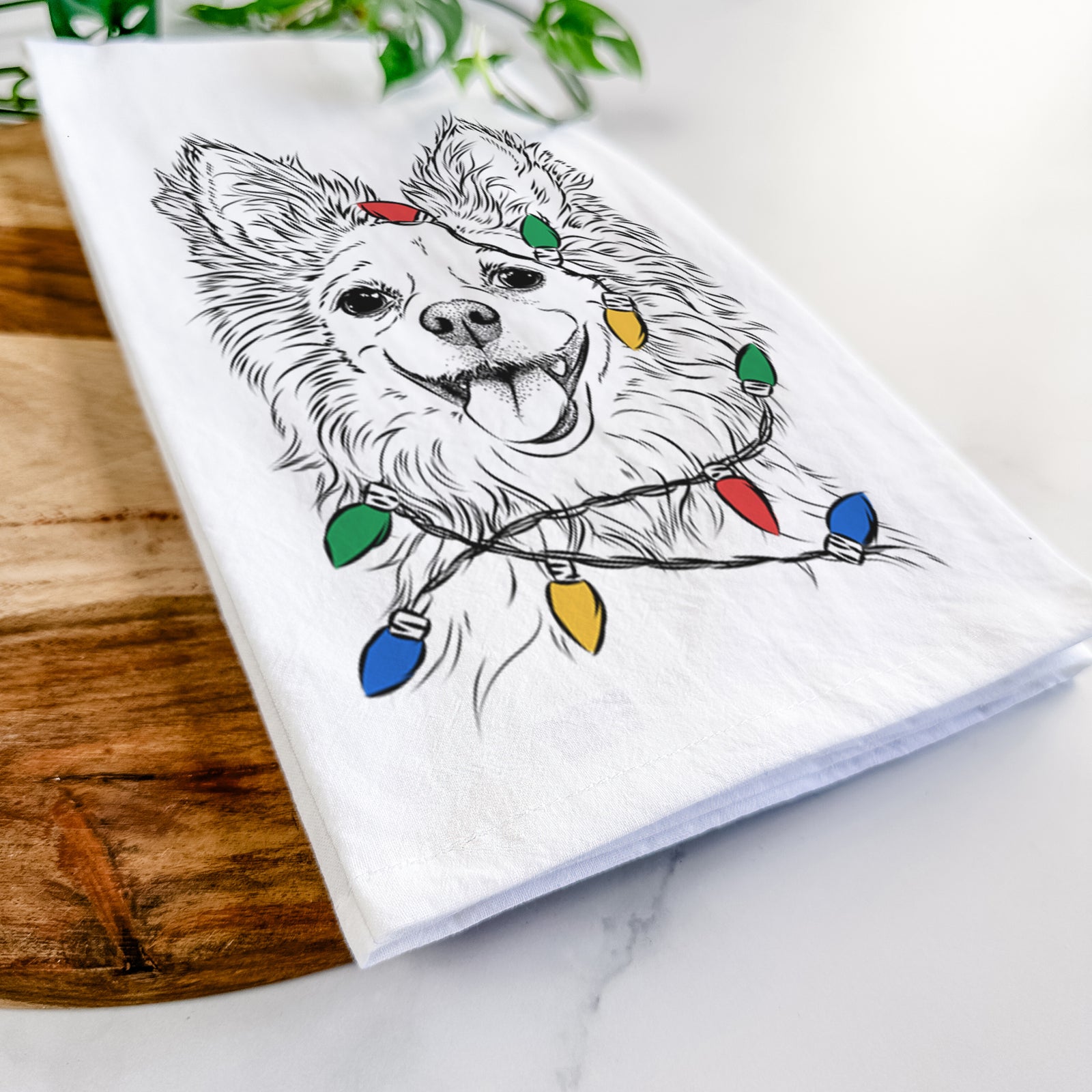 Hand-drawn sketch of Jasper the Pomchi wrapped in Christmas lights on a tea towel