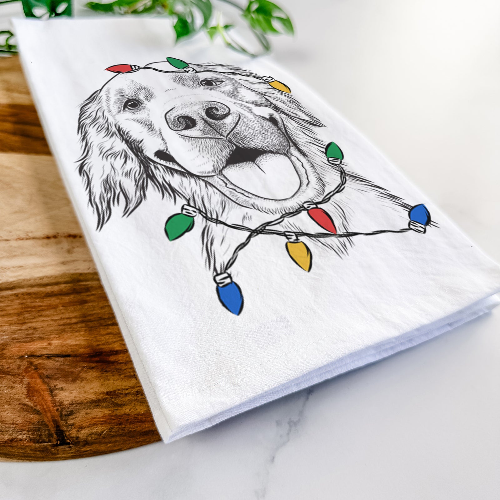 Hand-drawn sketch of Jordy the Golden Retriever wrapped in Christmas lights on a tea towel