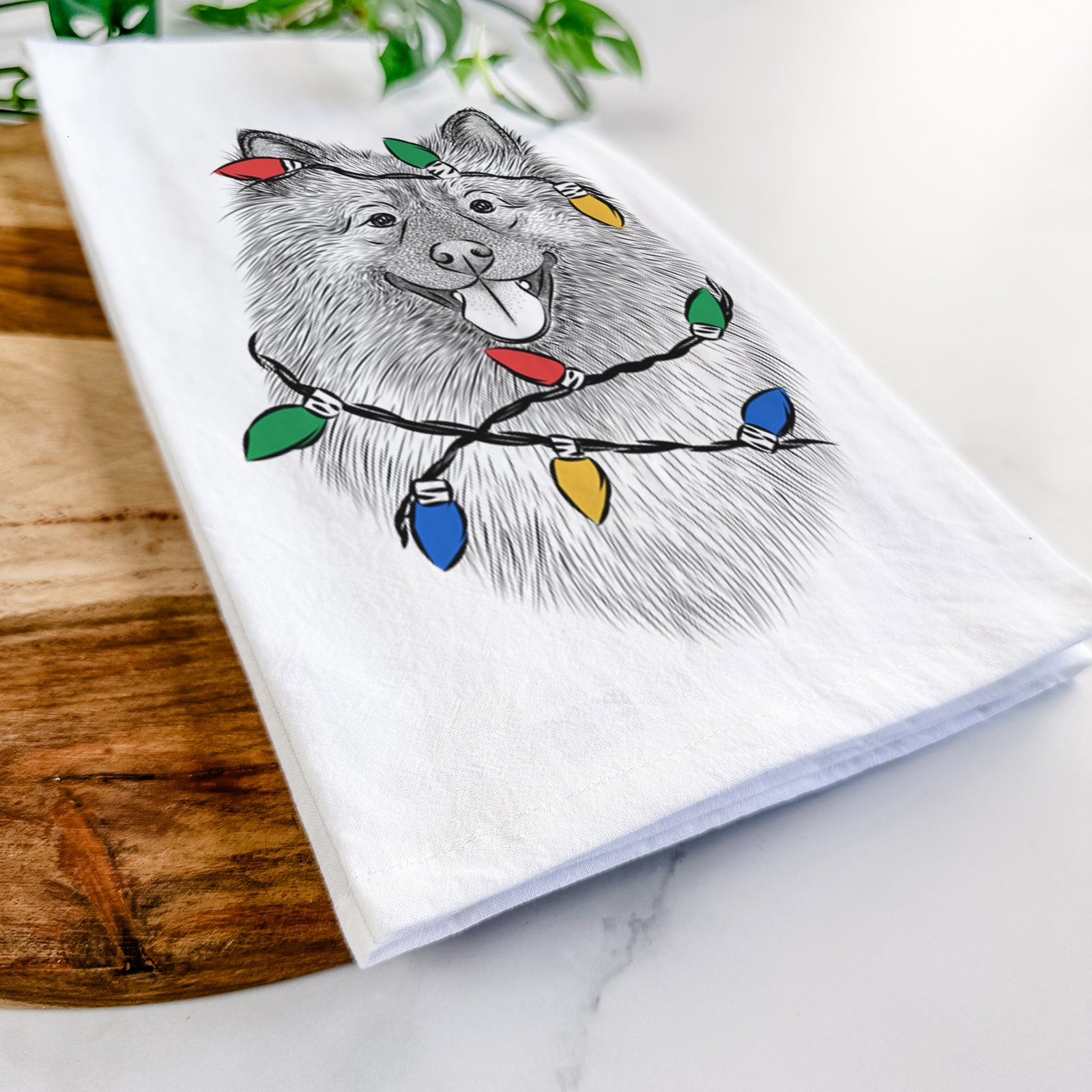Hand-drawn sketch of Kai the Keeshond wrapped in Christmas lights on a tea towel