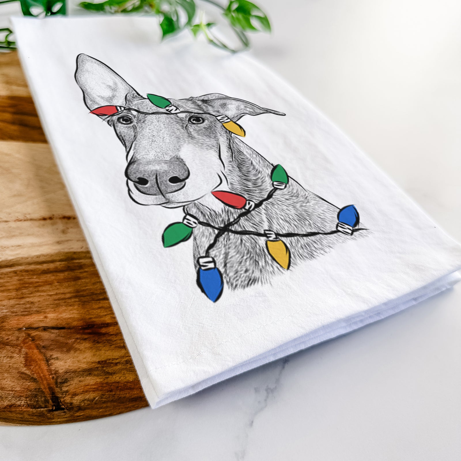 Hand-drawn sketch of Kain the Doberman Pinscher wrapped in Christmas lights on a tea towel